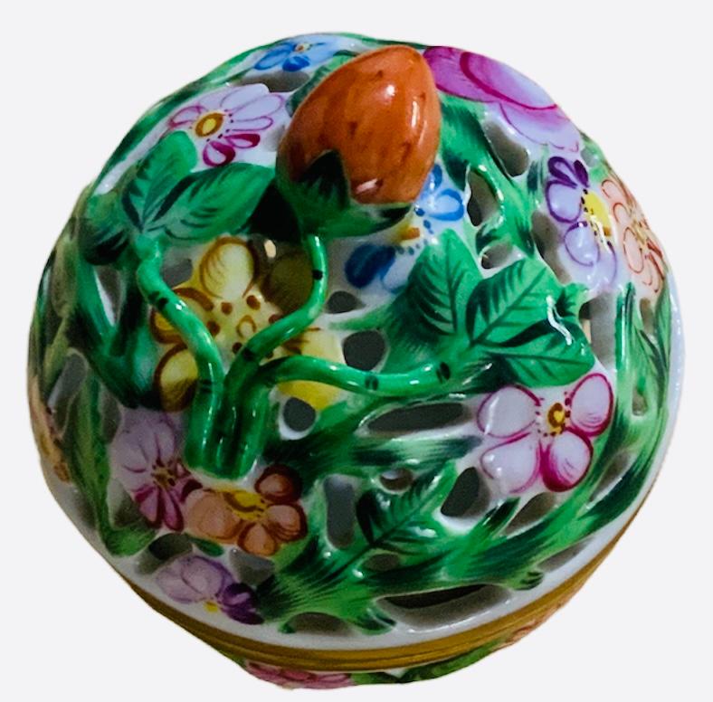 This is a Herend Porcelain reticulated round lidded potpourri box. It is hand painted with colorful flowers and green foliage. Its lid is decorated with a strawberry as a finial. Below its base is the Herend hallmark.