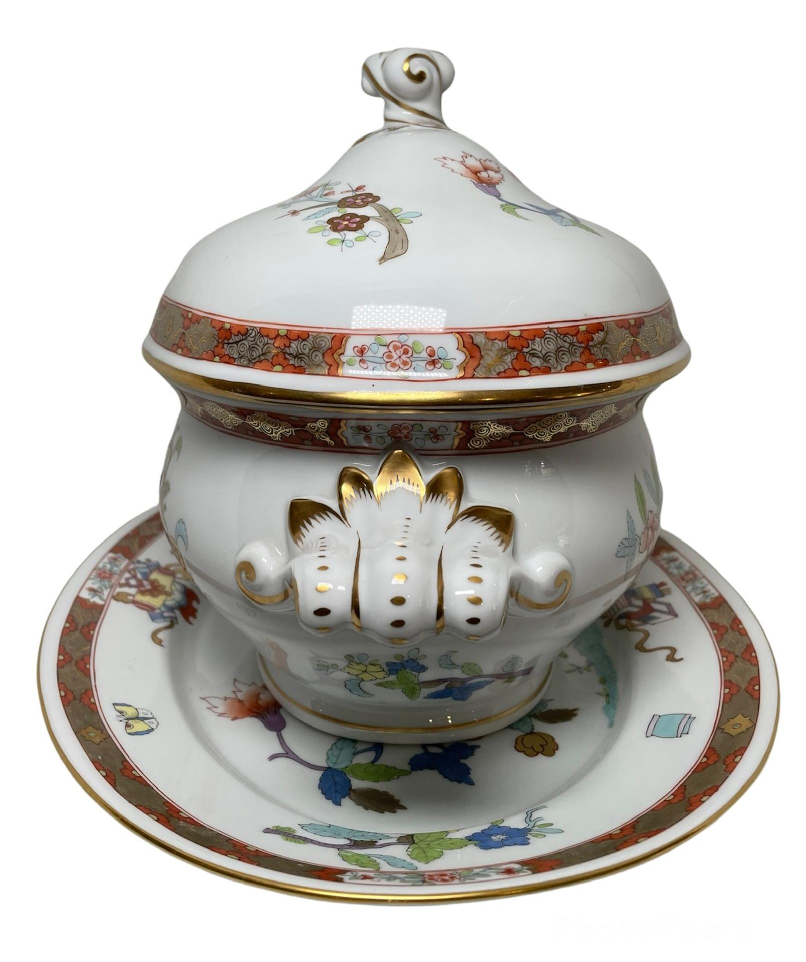 This is a Herend Porcelain Shanghai/Chinois pattern set of soup tureen and platter. It depicts an oval shaped bowl and large platter in a white background hand painted with different branches of polychromatic flowers and leaves. Both of their gilt