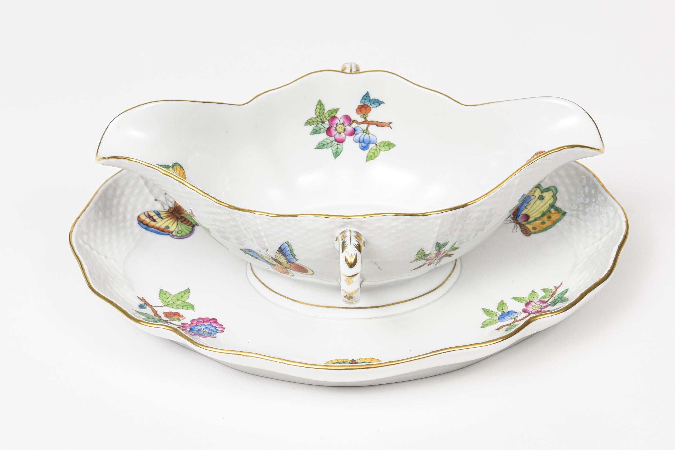 Elegant Herend China sauce gravy boat with attached underplate. This is the older pattern of Queen Victoria that does not have the green border. It has a weave rim and a gold edge. The pattern features flowers and butterflies.