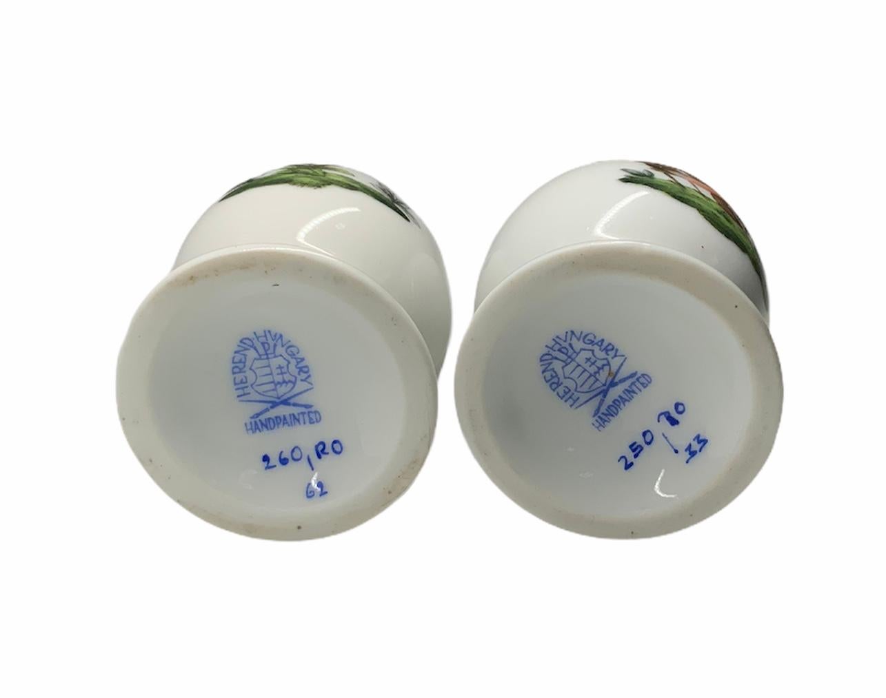 This is a Herend Rothschild pattern Hand Painted Porcelain of a pair of salt and pepper shakers. They are egg shaped with round pedestals attached to it that serve as stoppers. Their painting depict a scene with what appears to be a pair of warbler