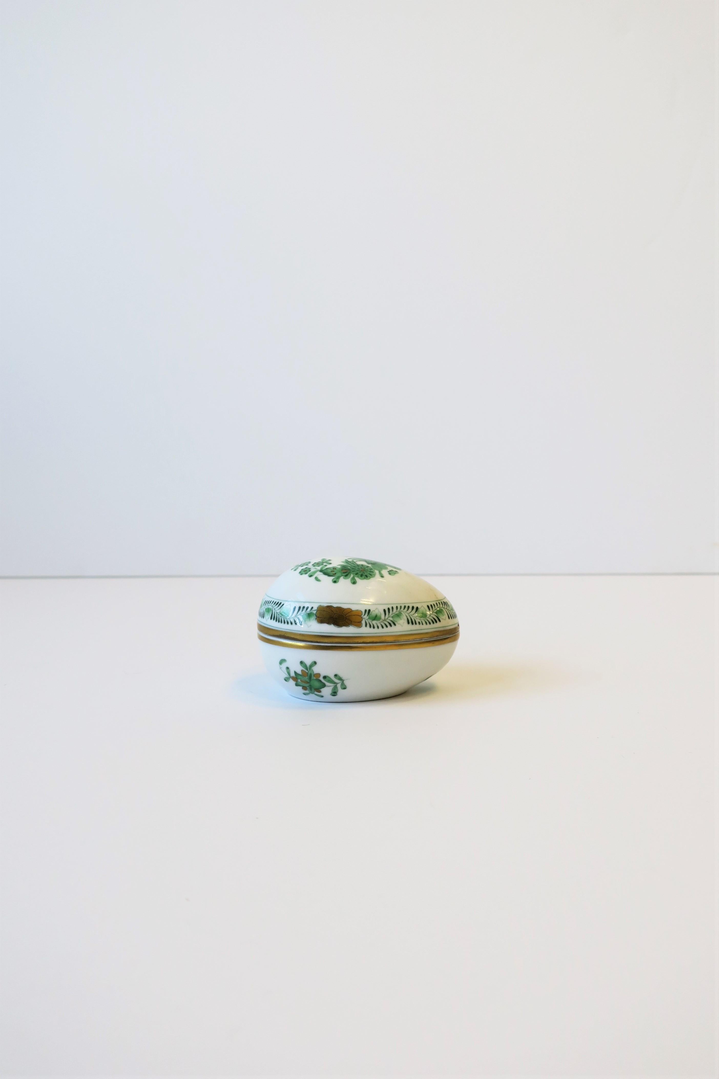 A beautiful white porcelain hand painted egg-shaped box from luxury maker HEREND, Hungary, circa 20th century. This Herend white porcelain egg-shaped box is hand painted by artist in emerald green and gold hues with a modern floral design. Box can