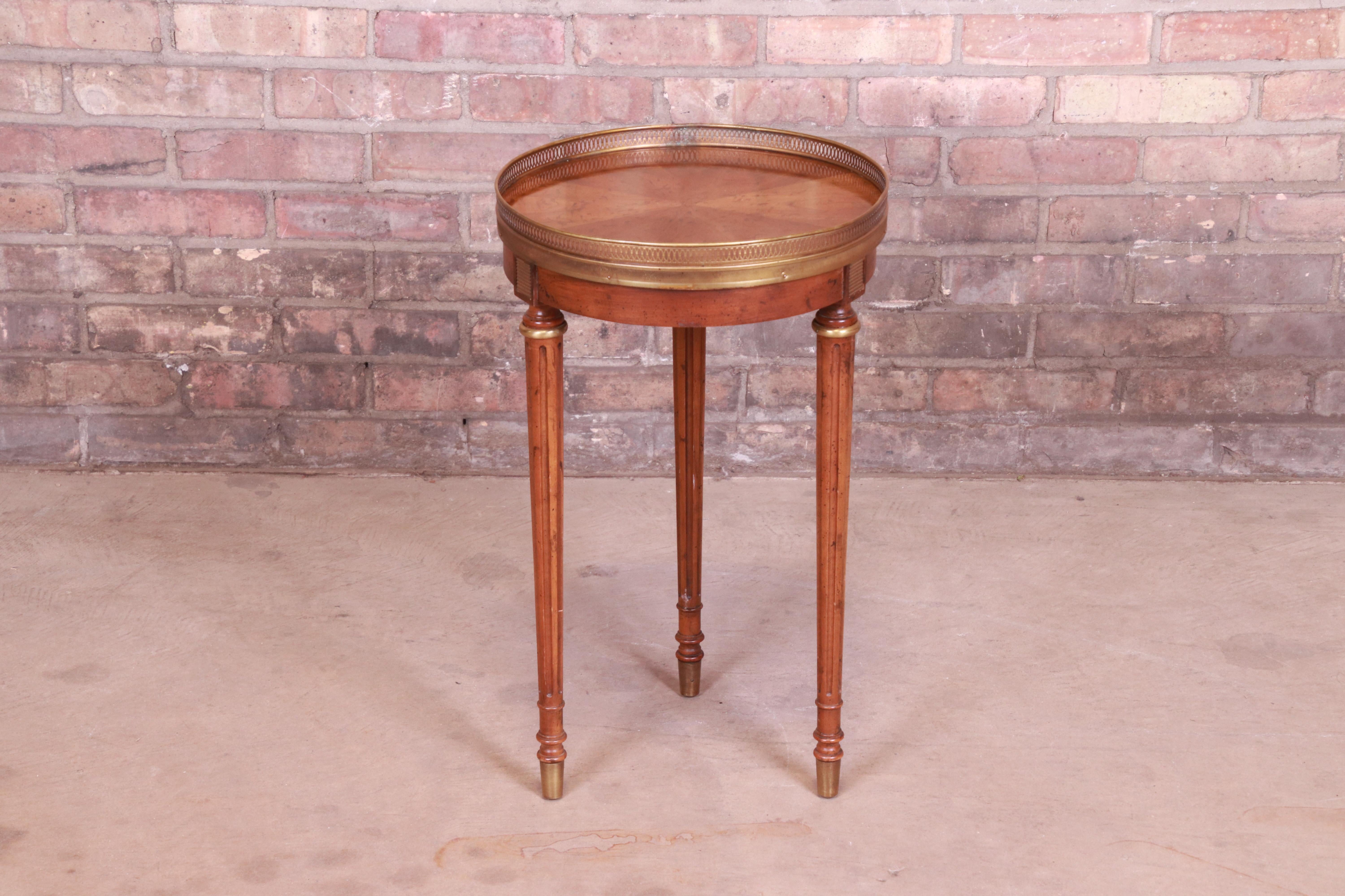 A gorgeous French Regency Louis XVI style tea table or occasional side table.

By Heritage Furniture,

USA, 1970s

Book-matched walnut top, with carved solid walnut legs, brass gallery, and brass sabots.

Measures: 13.88