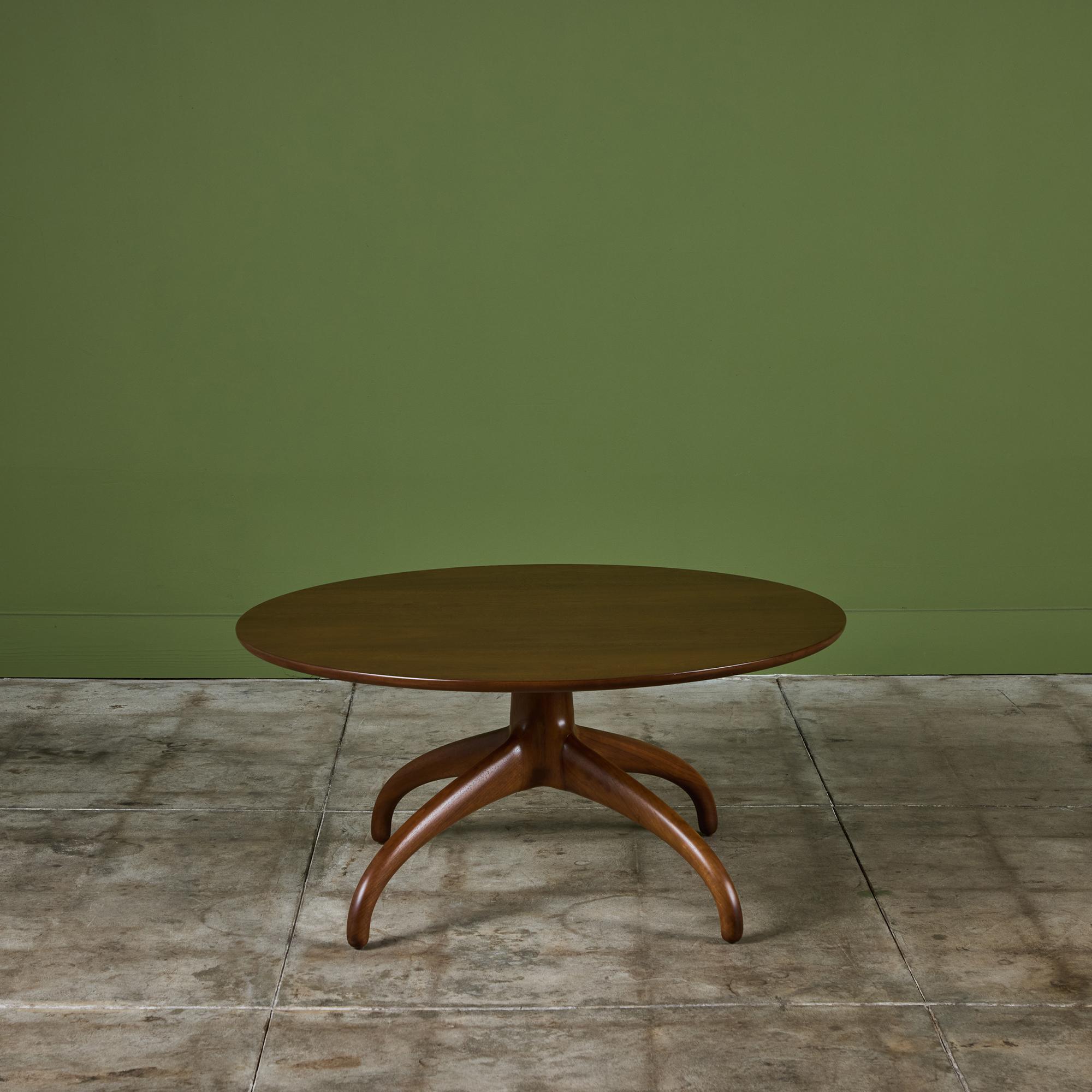 Table basse pour Heritage-Henredon, c.1960s, USA. La table présente un profil mince et un plateau rond en noyer. Le plateau est soutenu par quatre pieds sculptés de style 