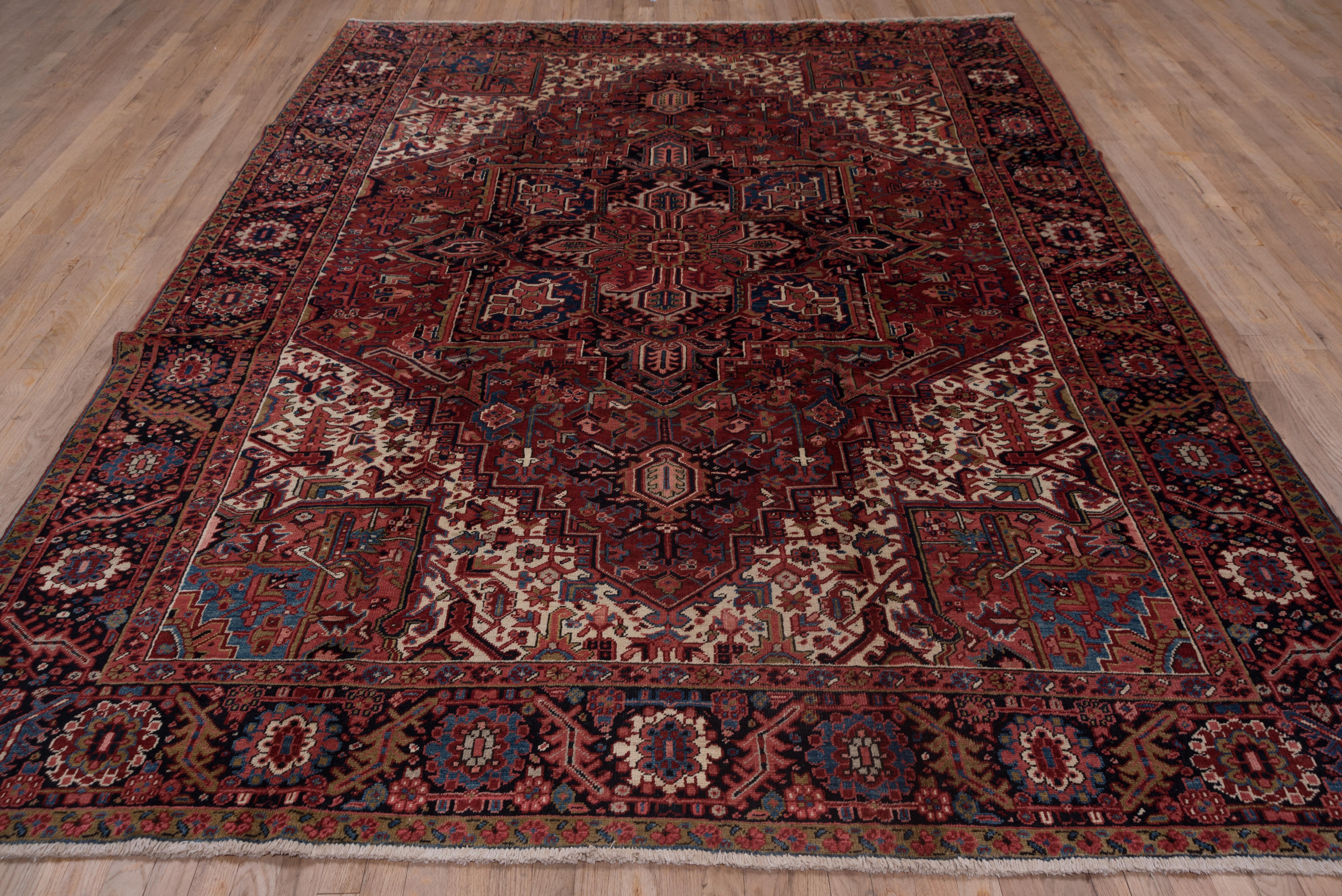 This elaborately drawn NW Persian carpet displays the classic navy palmette pendant octogramme medallion on a saturated red sub-field, set within densely patterned ivory extended corners with light blue cores. The navy border features bent leaves