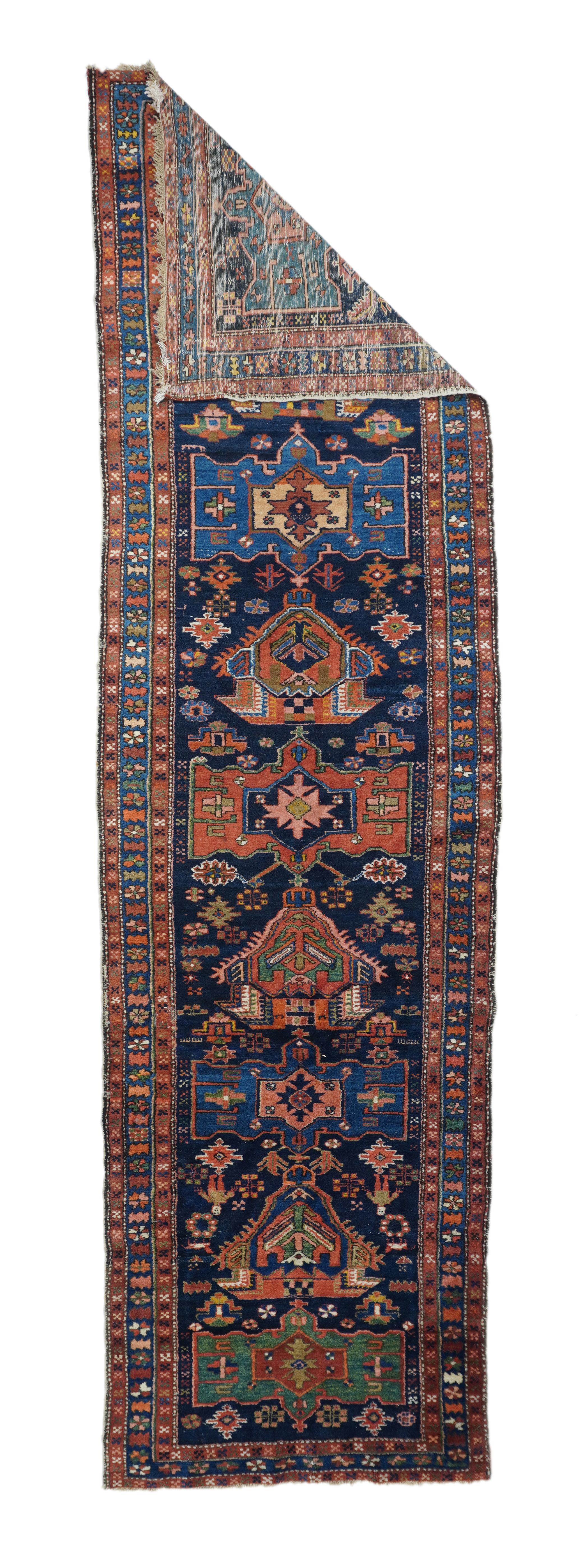 From the greater Heriz district in NW Persia, this kenare (runner) displays a central pole medallion of teal, rust and medium blue octogramme cartouches, alternating with barbed, one way palmettes in red and rust, all on the deep indigo round.