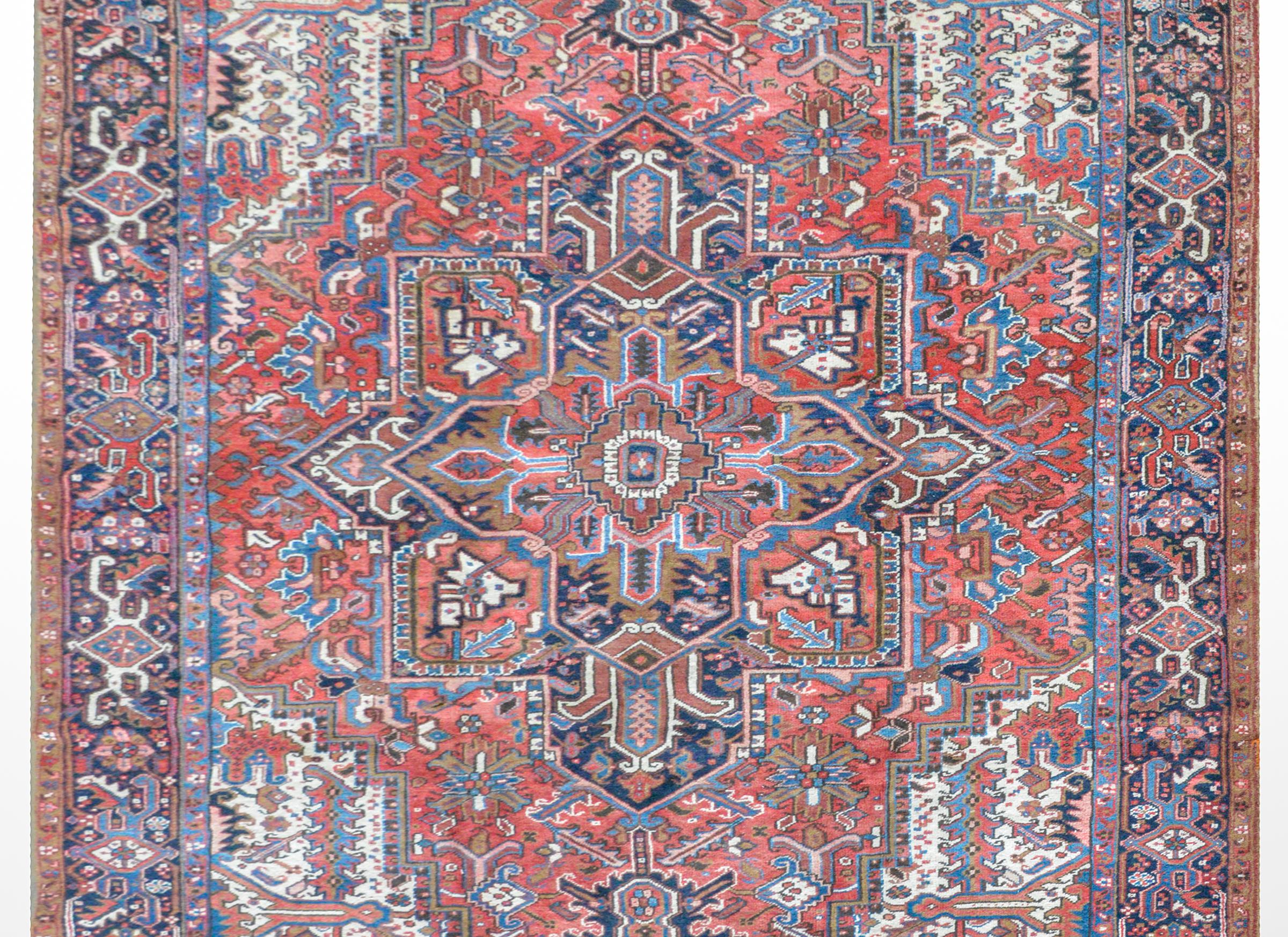 A wonderful vintage Heriz rug with a large central stylized floral medallion amidst a field of more flowers, leaves, and vines and surrounded by a wide floral pattered border, all woven in crimson, light and dark indigo, pink, brown, and white wool.