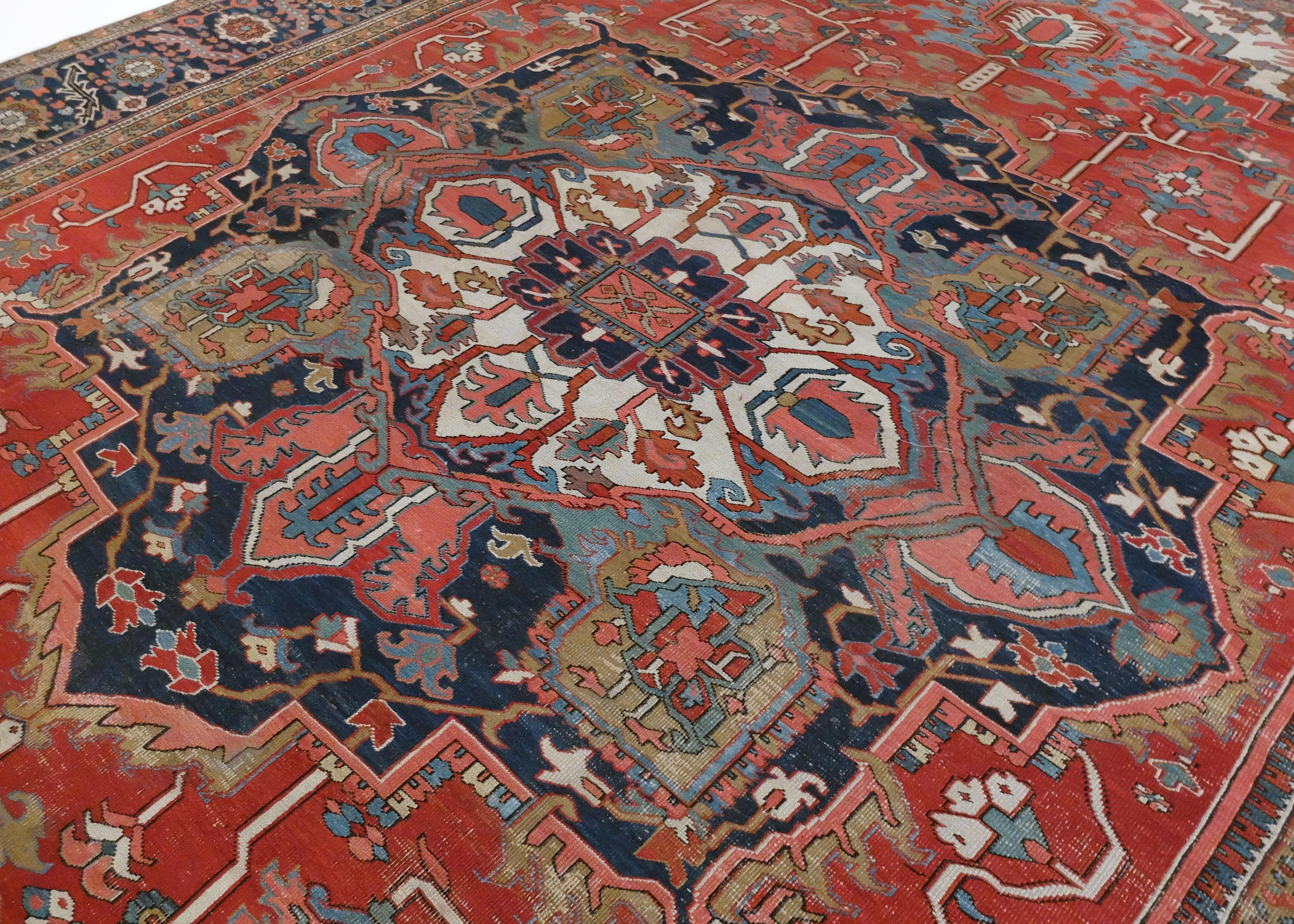 This is a Heriz rug made circa early 1900s. It has a large bold medallion in the middle surrounded by 4 bordering corner structures. The entire piece is highly stylized and consist of densely packed floral patterns. The colors are primarily reds,
