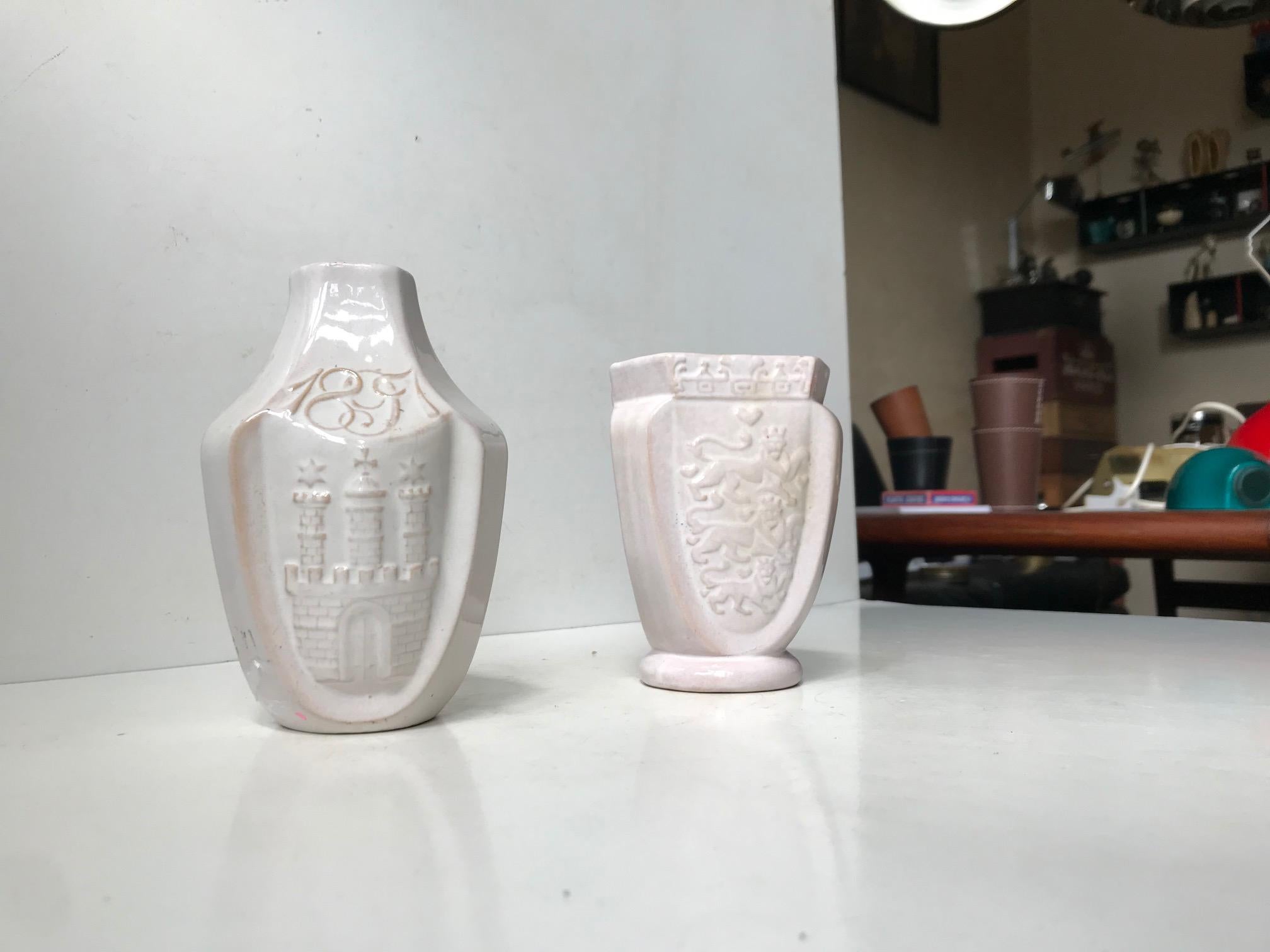 A set of pottery vases in delicate white glaze revealing the red clay underneath. Both decorated with relief motifs. One with the National Arms of Sweden, Norway and Denmark and one with important Scandinavian Castles to all sides. Both are hand