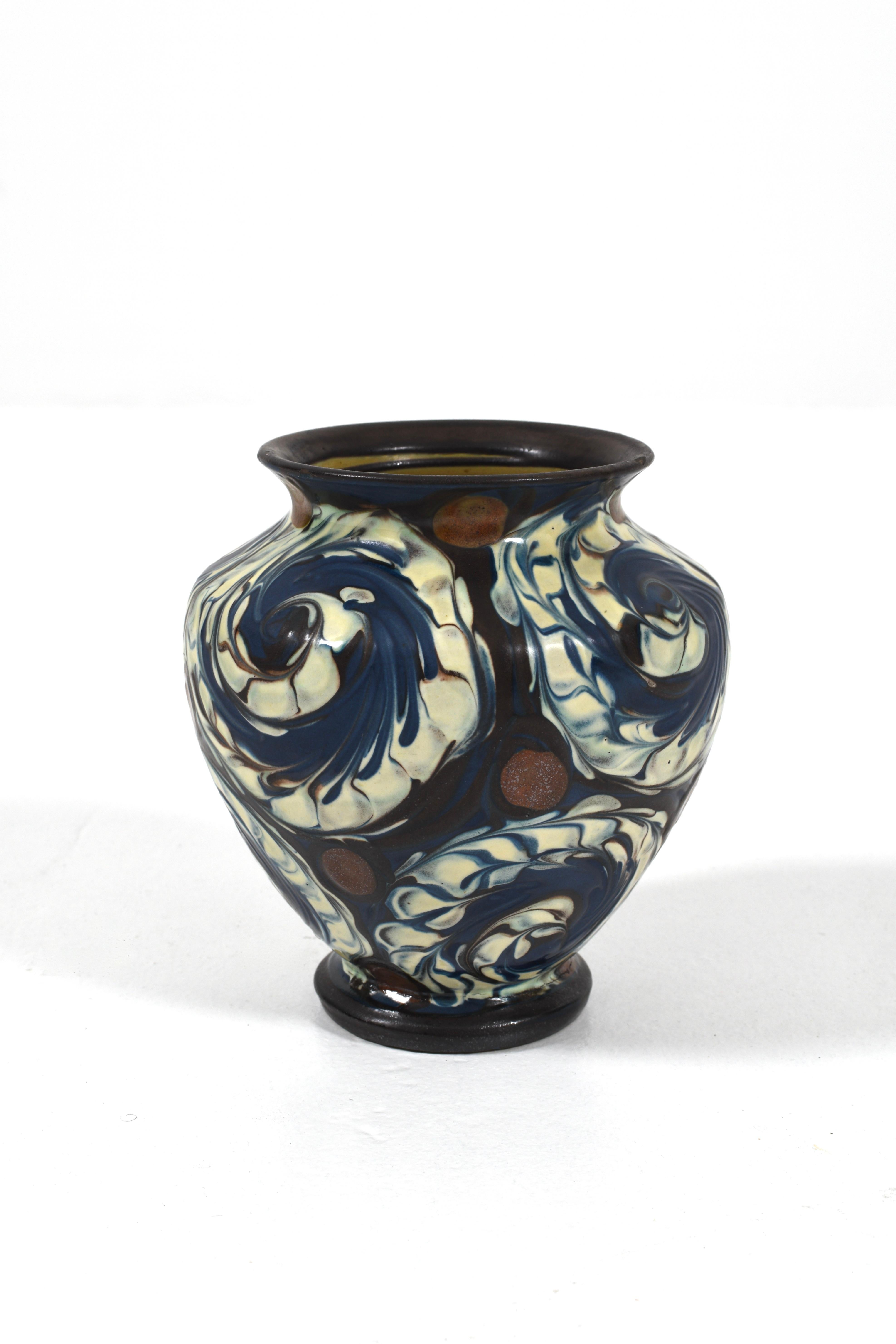 Splendidamente realizzato in Danimarca all'inizio degli anni '20, questo vaso Herman A. Kähler è caratterizzato da un'audace smaltatura a vortice nei colori blu intenso, avorio e terracotta. La sua forma arrotondata e il bordo svasato evidenziano