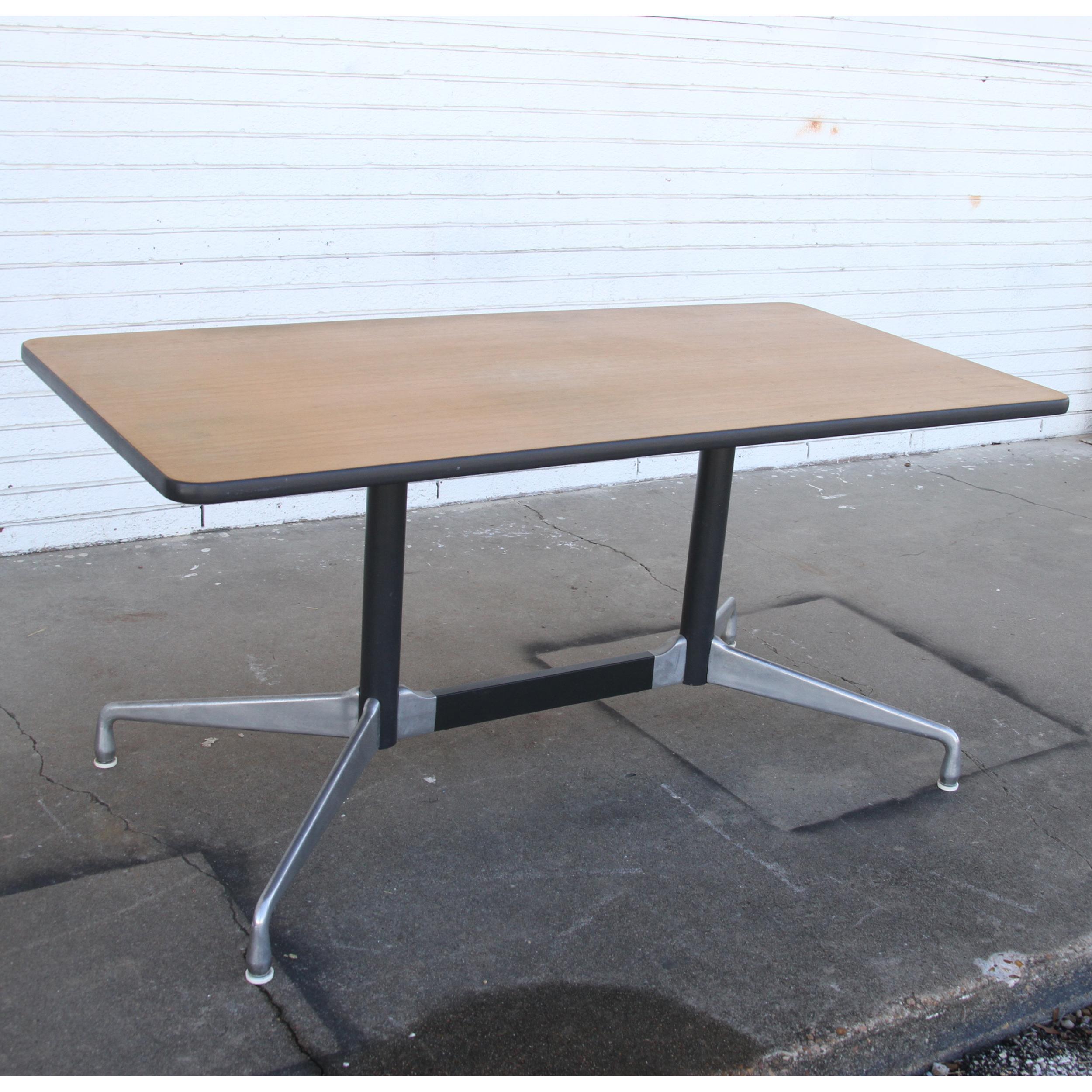 Il s'agit d'une table de conférence/dîner Herman Miller avec un plateau rectangulaire. Le plateau est en noyer. La base emblématique a des pieds qui sont construits en acier et les pieds en aluminium brossé. La base est conçue pour accueillir des