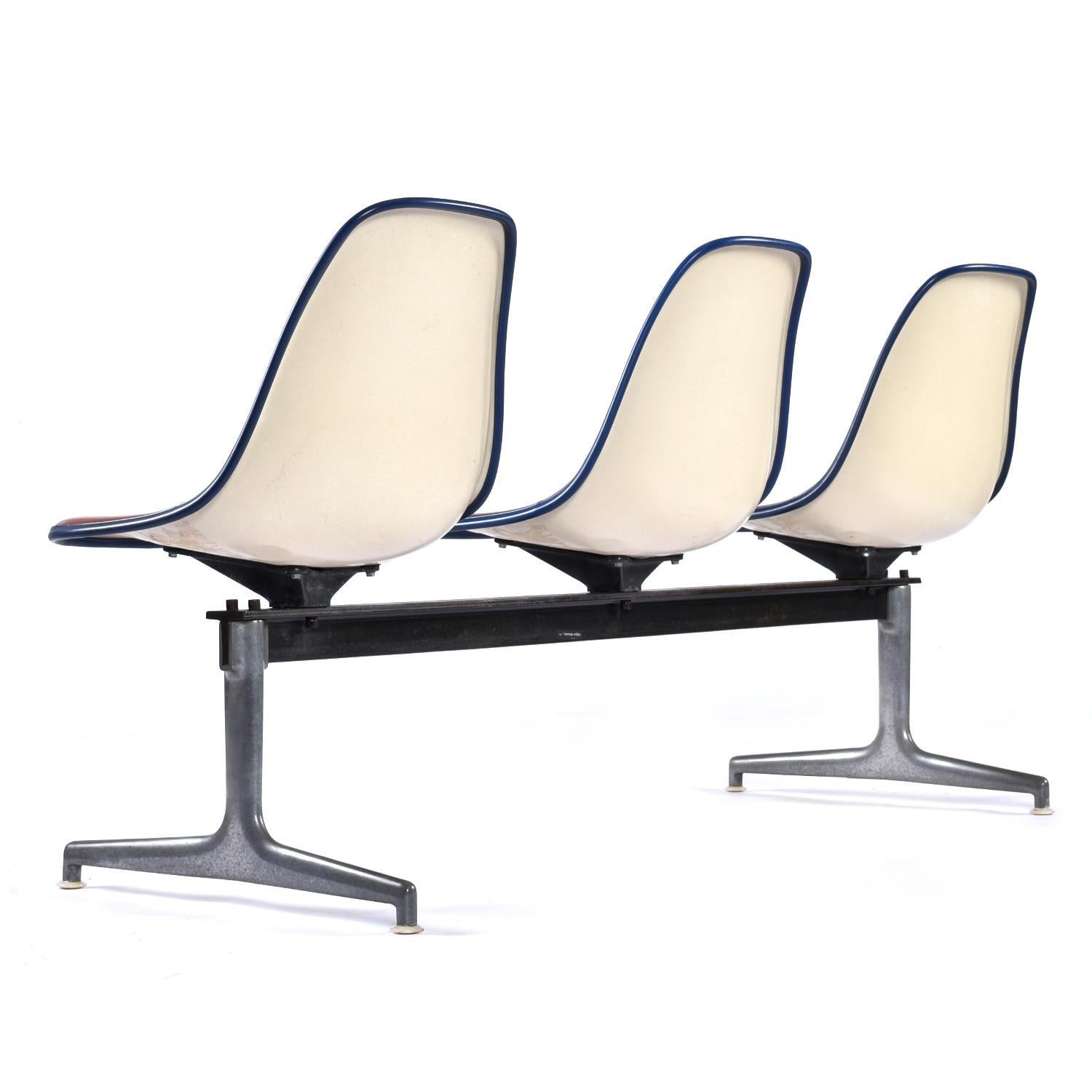 Iconic Mid-Century Modern Charles and Ray Eames for Herman Miller tandem bench. This modular system features three Eames shell chairs with red/orange colored original Naugahyde pads. These unique original Naugahyde pads are a orange-tinged red