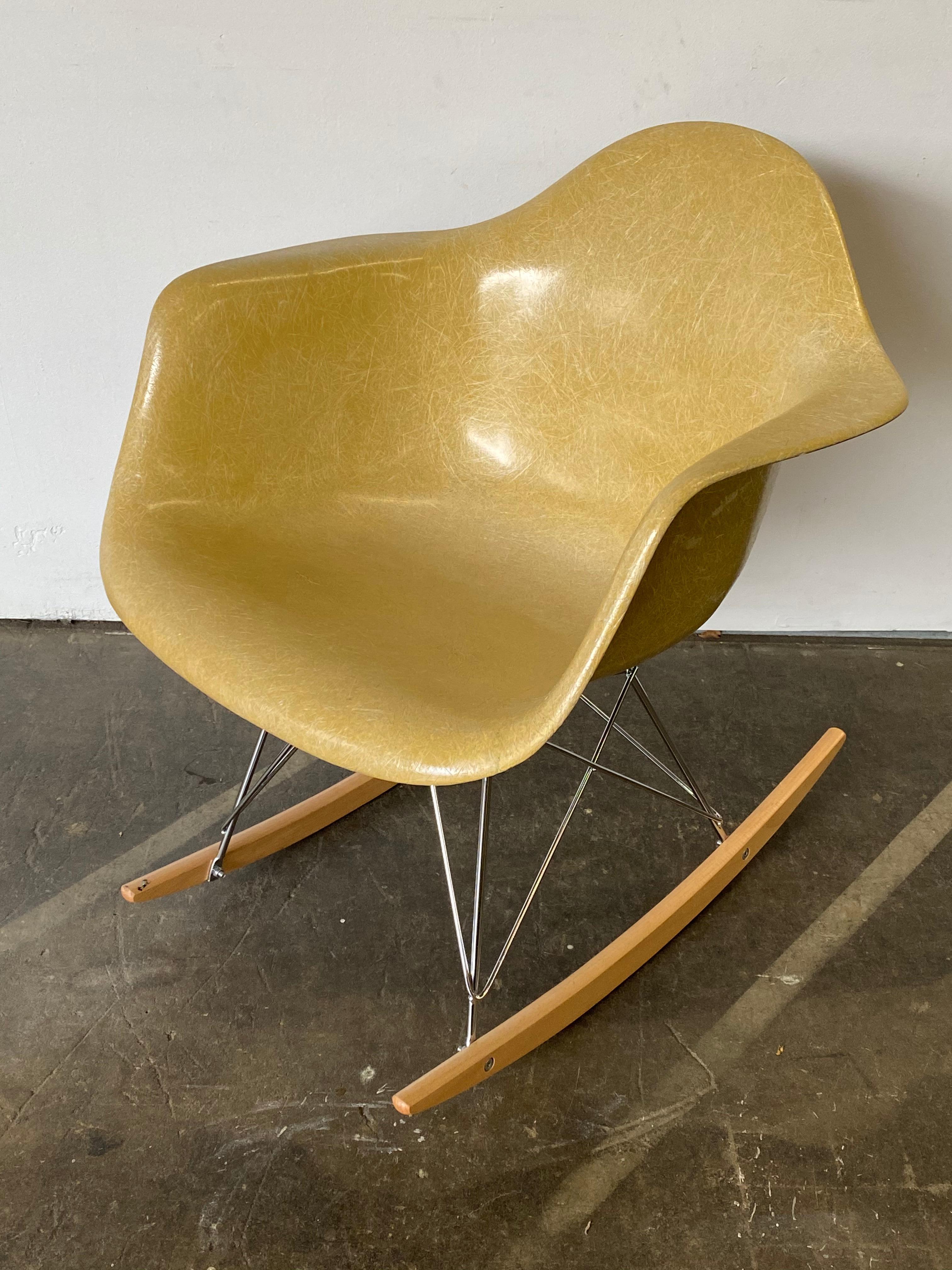 Eames rocking chair in ochre light. Made by Herman Miller and stamped underneath the seat. This chair radiates well-worn vintage charm but does show its history and age. Slight fading in the seat. Stamped Herman Miller and guaranteed authentic. Base