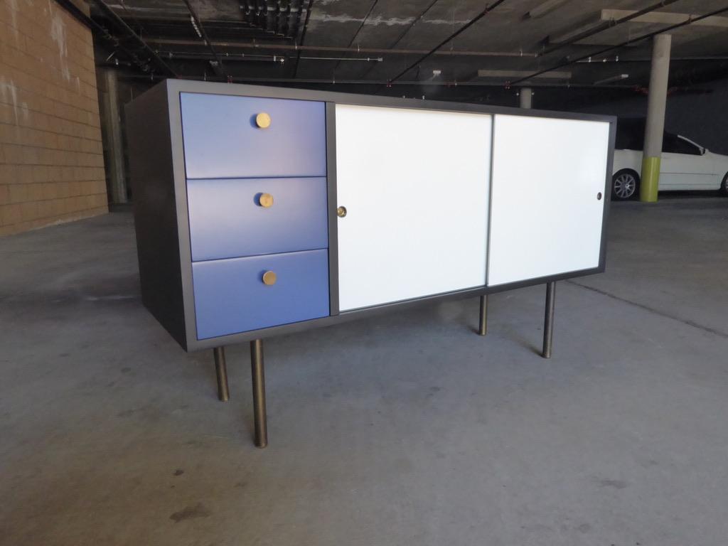 A charming 1960s multi-color painted low cabinet/chest in the style of Eames for Herman Miller. The doors slide open to reveal a single shelf and on the right side of the cabinet are three drawers with brass pulls. The legs are also made of brass