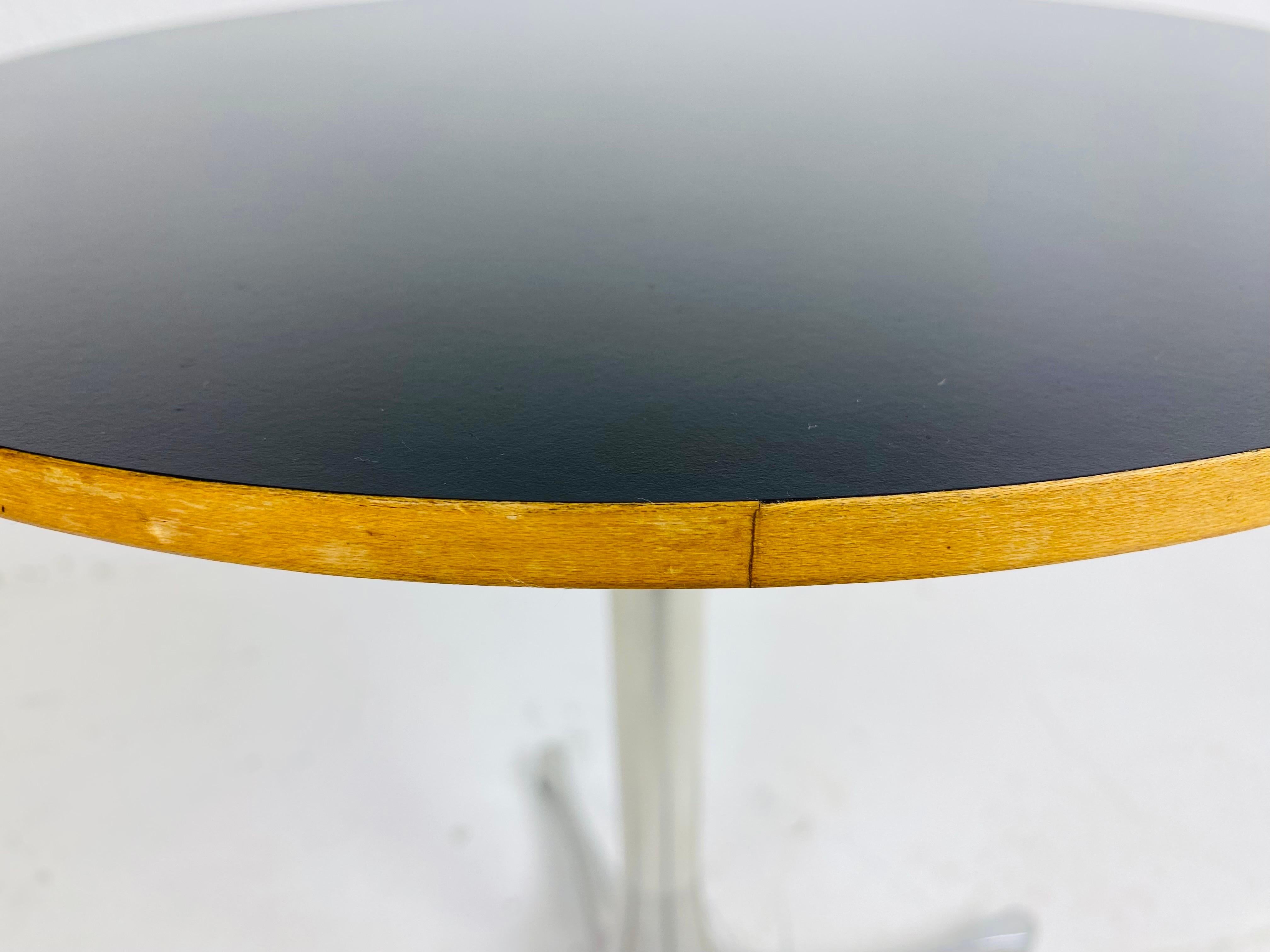 This is a mid century modern Diminutive martini table by Herman Miller. This martini table has a black laminate top with a dark walnut finished edge. The base is chrome with four expanded legs. This is a classic Herman Miller table circa 1970.