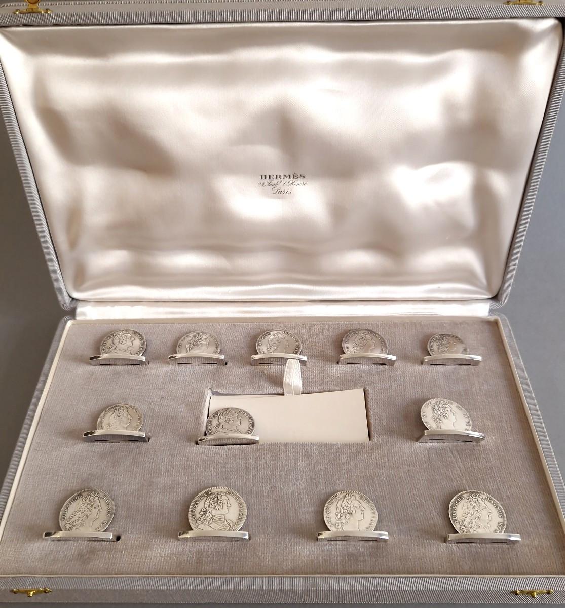 12 Sterling Silver place card holders from Maison Hermès
Each one made from a coin depicting Louis XV
Silver hallmark with boar's head
Signed Hermès Paris on each
Length: 3.6 cm
Width: 2 cm
Height: 2.8 cm
Weight: 347 grams
In its original case