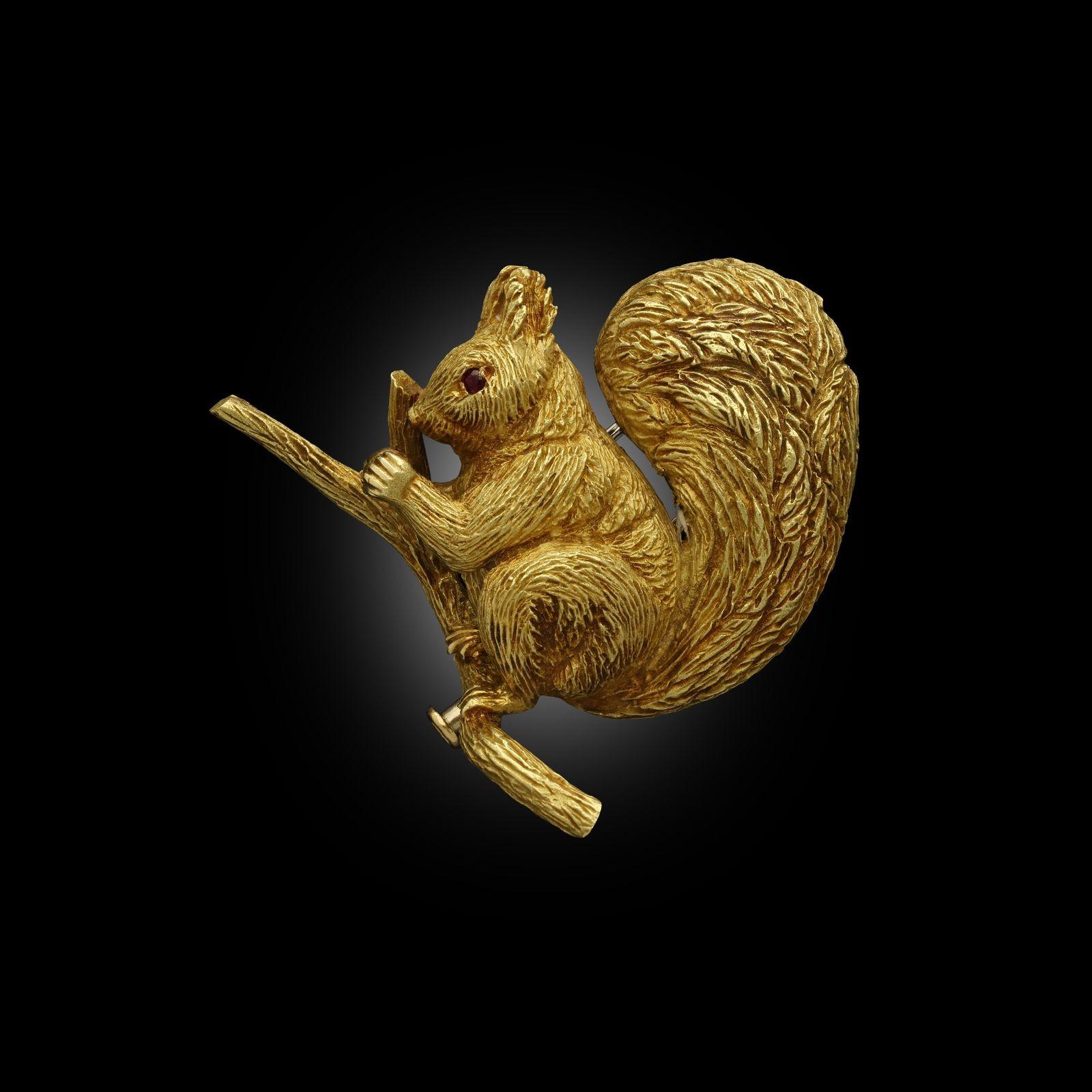 Die dreidimensionale Brosche ist in 18-karätigem Gelbgold fein modelliert und zeigt ein Eichhörnchen, das auf einem Ast sitzt und eine Nuss zwischen den Pfoten hält. Der Körper und der große aufrechte Schwanz sind sorgfältig strukturiert, um das