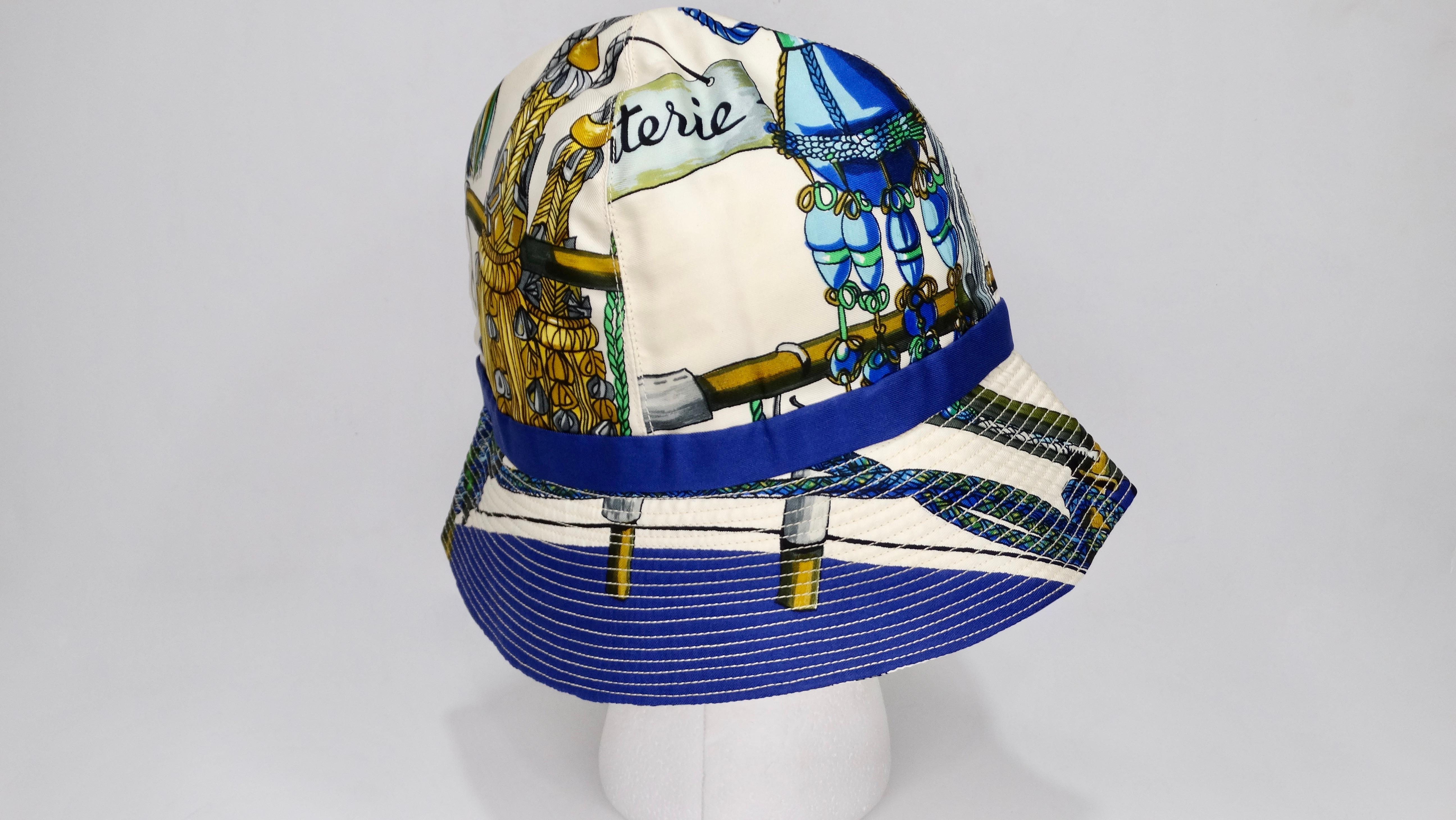 Pour tous les amoureux d'Hermés ! Ce chapeau seau est orné de l'écharpe Passementerie Hermes conçue par Françoise Heron en 1960, qui met à l'honneur l'art de la fabrication traditionnelle des glands. L'écharpe complète comporte une série de glands