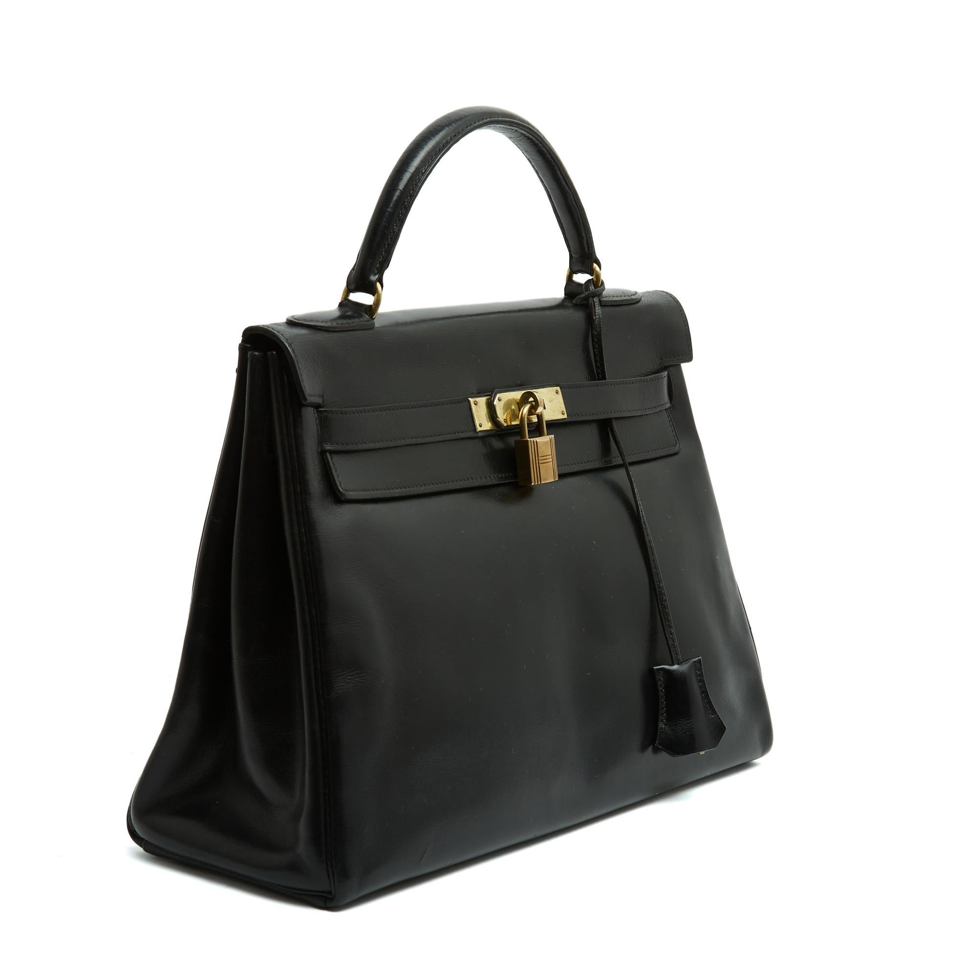 Borsa Hermès Kelly, taglia 32, in pelle nera e finiture dorate. L'interno è foderato in pelle nera con due tasche e una grande tasca (non chiusa da zip). Include un lucchetto, chiavi, clochette e linguetta (originale). Sul retro di una delle cinghie