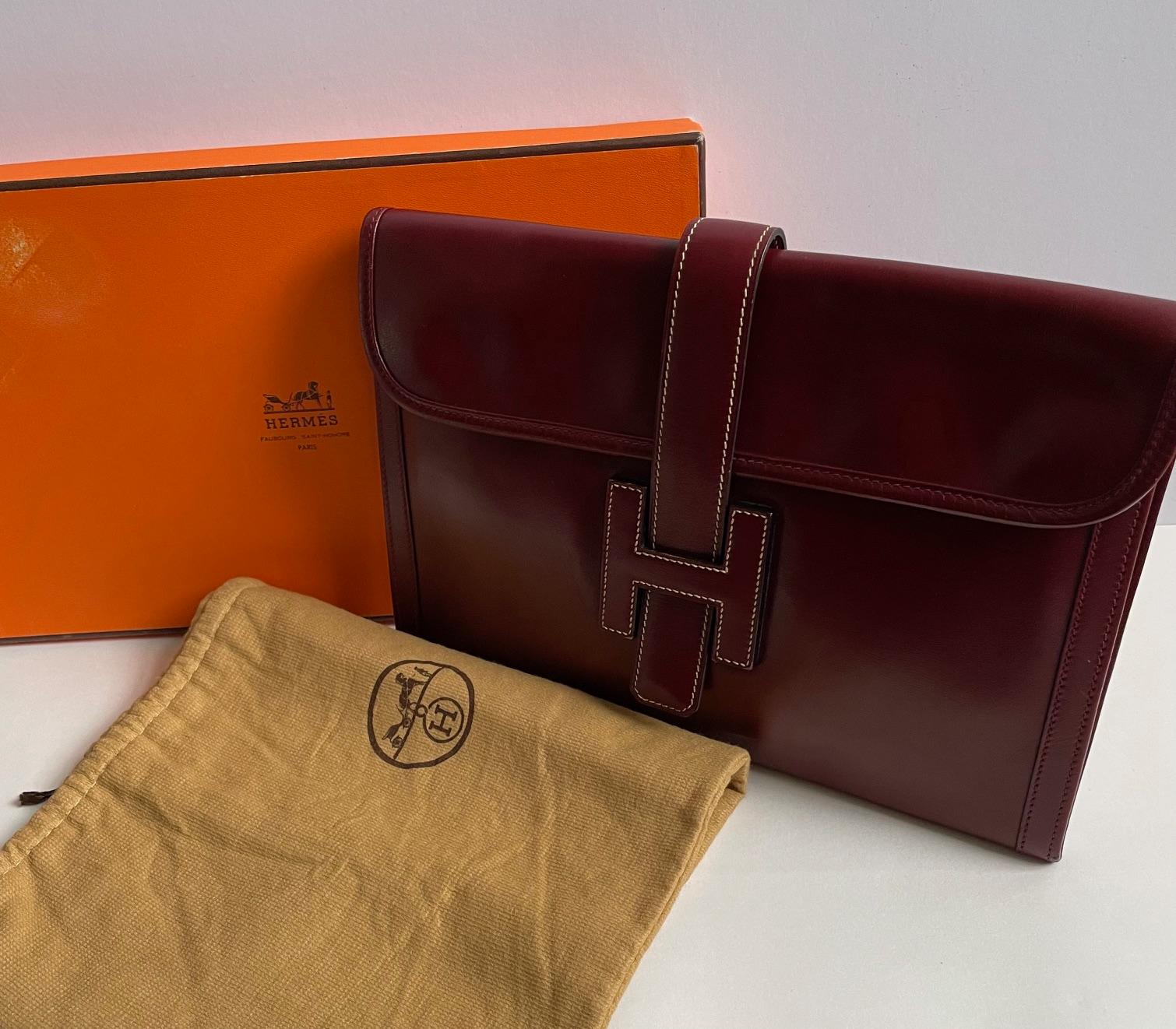 HERMÈS 1979 Jige Clutch Box Leather Vintage W/Box. A timeless vintage 1979 Hermès Jige pochette clutch in Burgundy deep red box leather with off-white stitching and saddle red stitching. Large H closure on the flap, off-white beige canvas interior