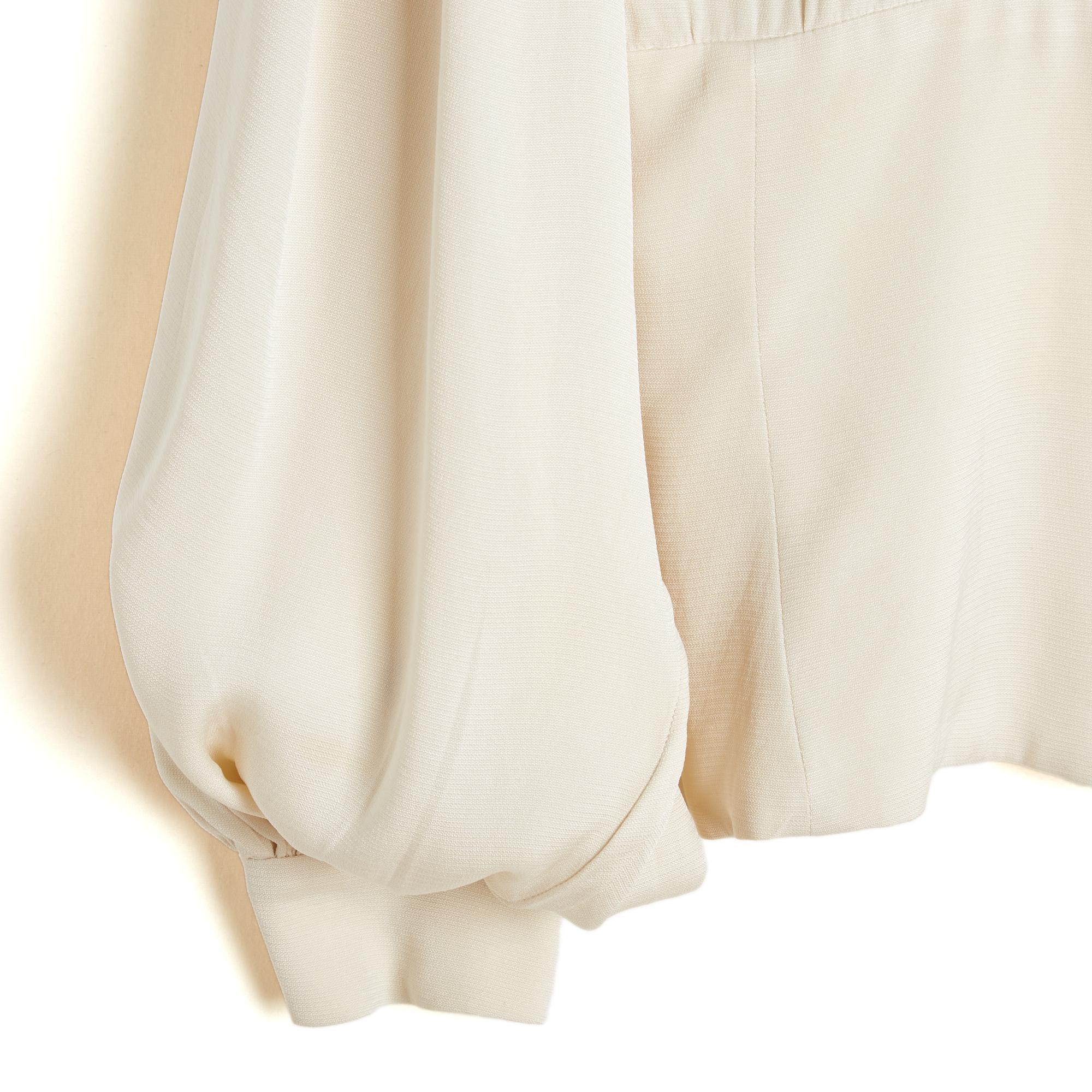 Hermès top blouse circa 1990 in ecru silk crepe, collar closed by 7 buttons including 1 hidden under the collar, 3 hidden in the upper part and 3 visible on the fitted waist, all with Hermès logo, long puffed sleeves closed by a matching button.