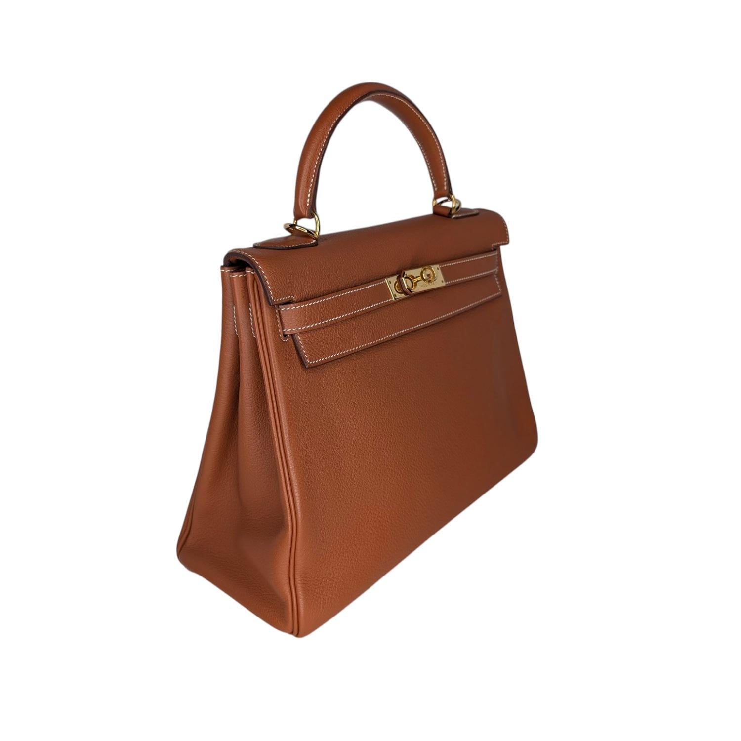 Cartable Hermès 2004 Clemence Kelly Retourne 28 Or

Cette sacoche Hermès est magnifiquement réalisée en cuir Clémence estampillé en or. Une poignée unique en cuir roulé est fixée à l'aide de ferrures en plaqué or poli. La traditionnelle bascule