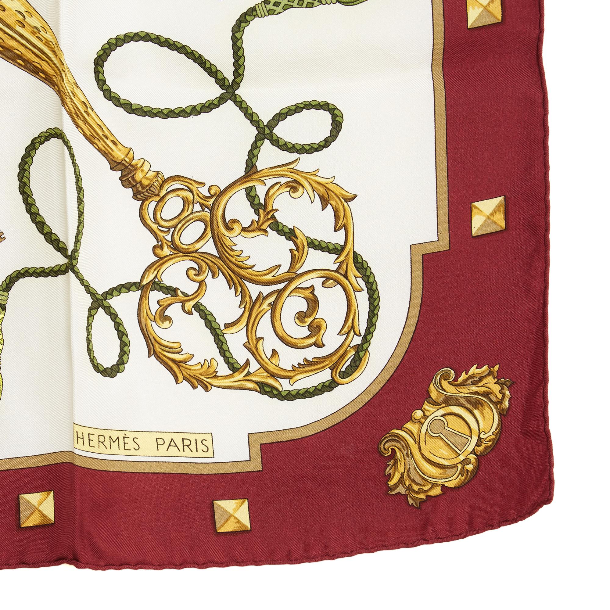 Foulard quadrato di Hermès, taglia 90, in twill di seta, disegno Les Clés di Cathy Latham, prodotto per la prima volta nel 1965 e riedito nel 1980 e nel 2010 (come questo), nei toni dell'oro su sfondo ecru, con bordo bordeaux. Circa 90 cm di