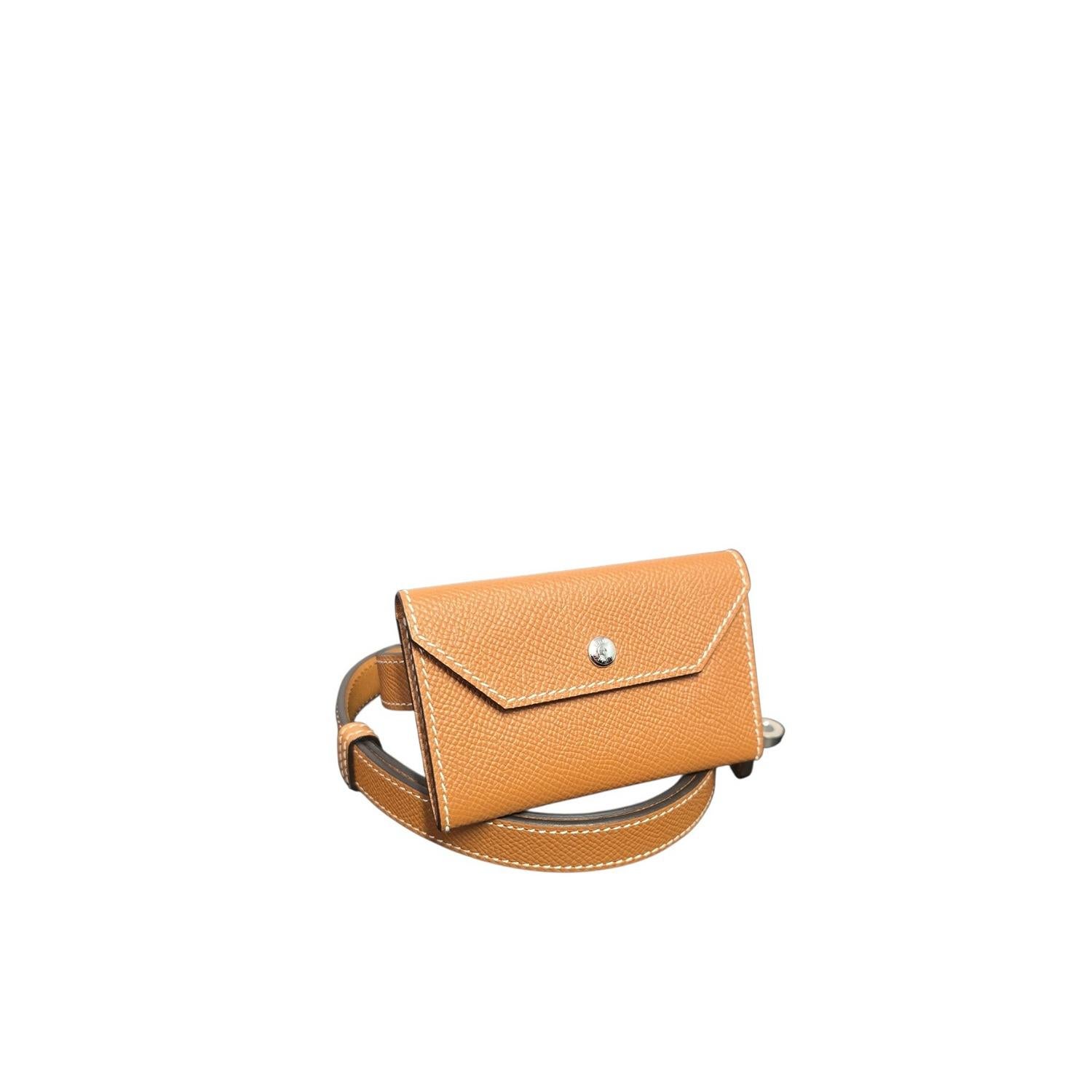 Questa elegante e versatile cintura Hermès con mini-portafoglio è realizzata in resistente pelle di vitello Gold Epsom e presenta finiture lucide placcate Palladio. Accessorio perfetto per uno stile a mani libere, questa cintura può essere regolata