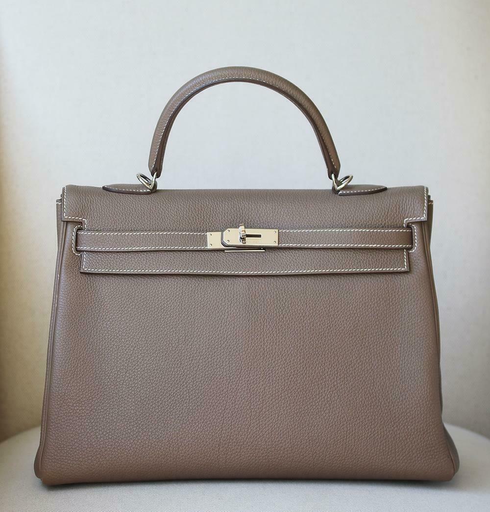 This extremely beautiful Hermès Kelly Retourne 35 Togo Bag in Etoupe with Palladium Hardware is a must have for your collection! 
The beautiful subtle earthy-tone exterior of the bag works well with every outfit. Contrast stitching.
The bag is