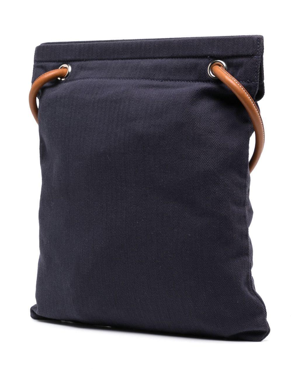 Le sac Hermès Aline a été conçu pour faciliter la vie des cavaliers et leur fournir un moyen de tenir et de transporter facilement selles, bottes et brosses. Confectionnée en coton bleu marine, cette pochette porte la marque 