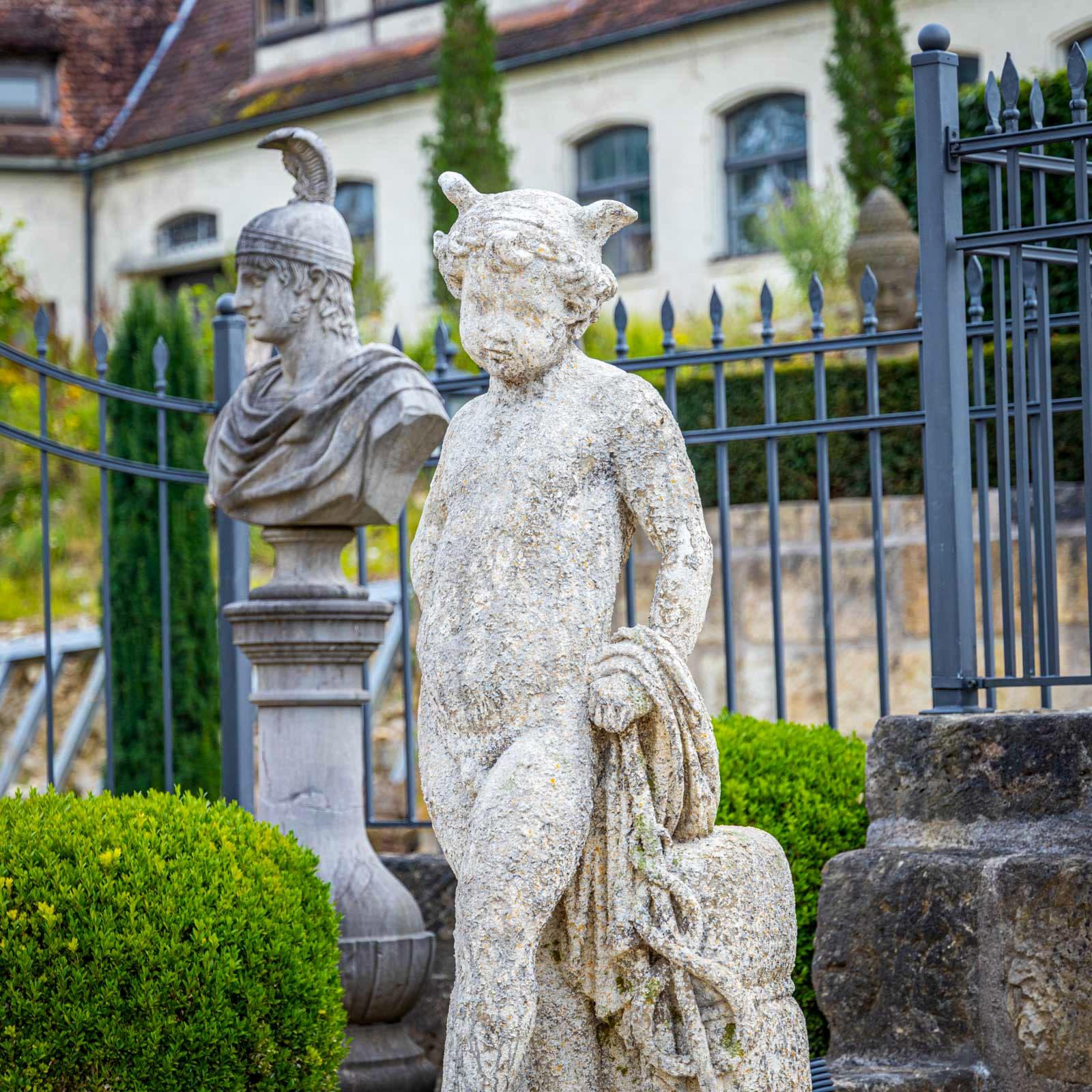 Life-size cast stone figure of Hermes with Aesculapian staff and winged helmet. He is leaning casually against a small wall. The sculpture has a beautiful natural patina. 