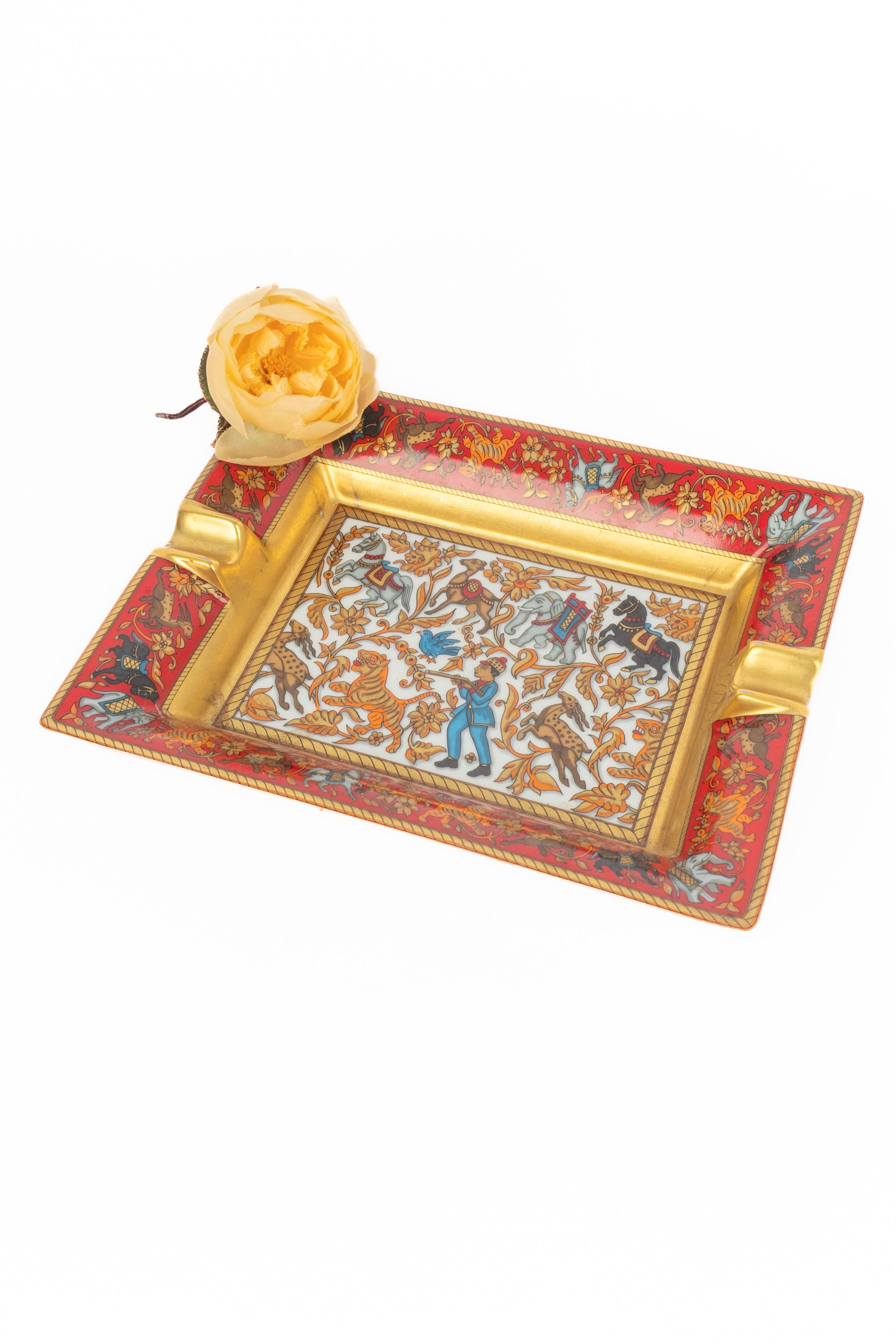 HERMÈS - (Made in France) Limoges porcelain ashtray / coin tray. 'Hunting in India' ('Chasse En Inde') design in red, golden, and blue tones. Tray base protected with a velvet goat skin.

Condition:
Good condition

Dimensions:
Length: 20 cm - Width: