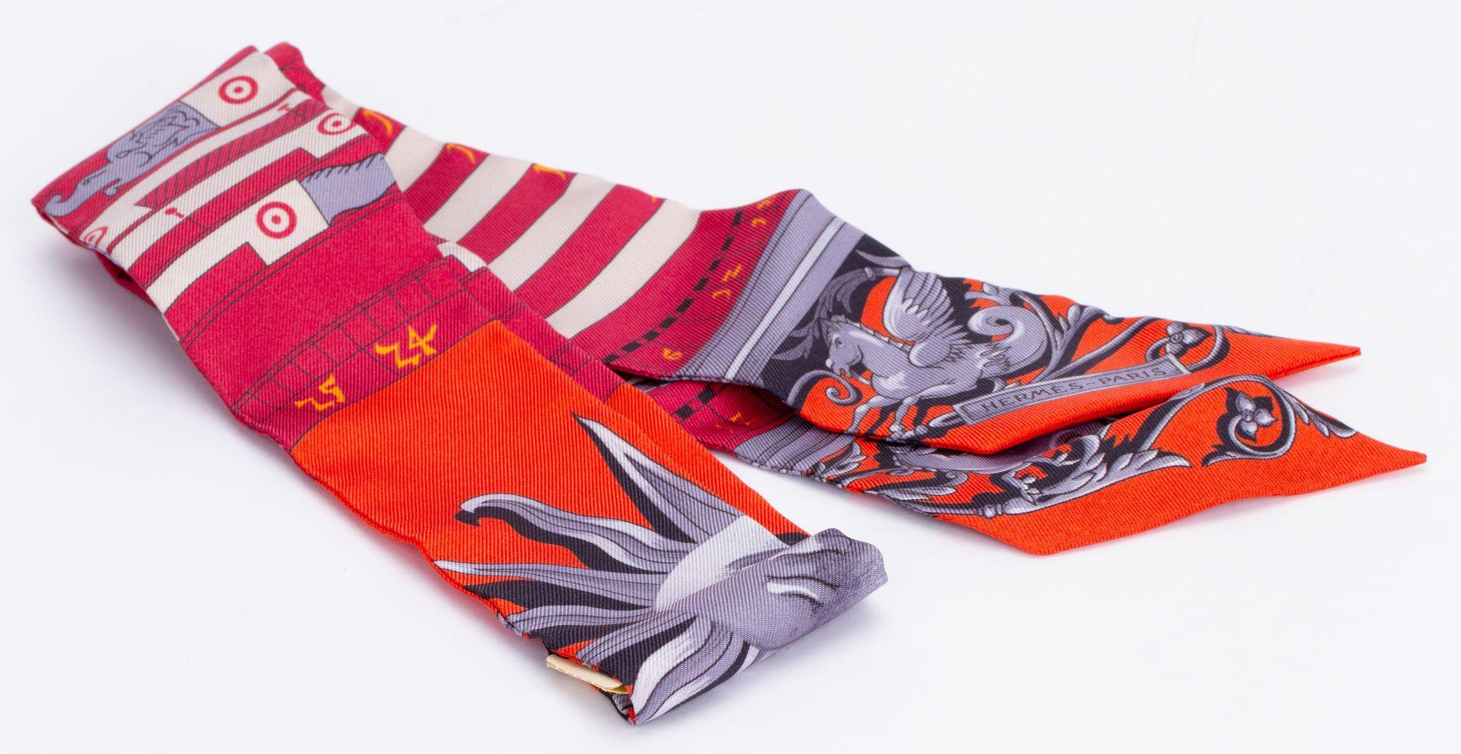 New Hermès Sun Twilly. The scarf is made out of silk and the main color is red. The print shows a sun in grey. The piece comes with a scarf ring. It is packed in the original box and ribbon.