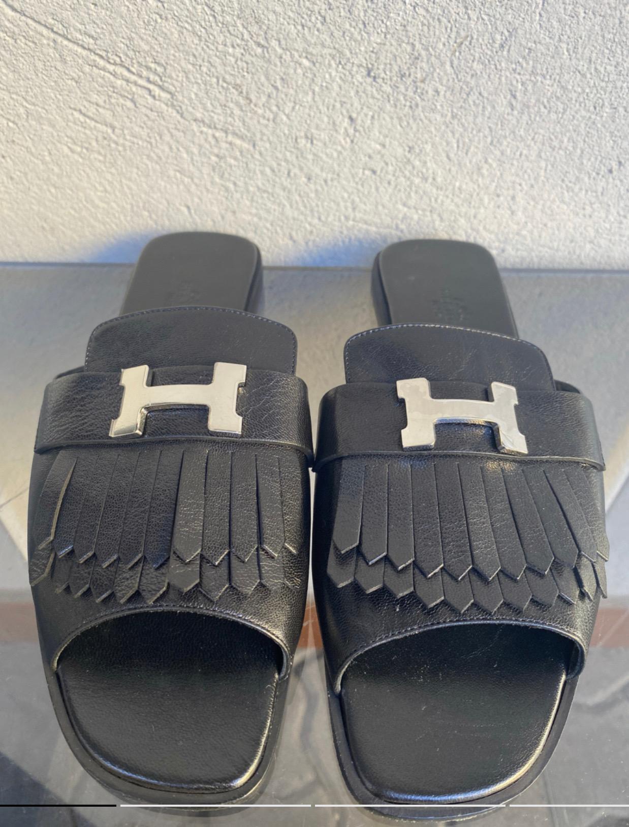 Hermes Auteuil flat sandal, in black leather, with silver-colored steel logo, with fringes. Heel height 1.5 cm, internal insole length 25 cm, in perfect condition, new, never worn.