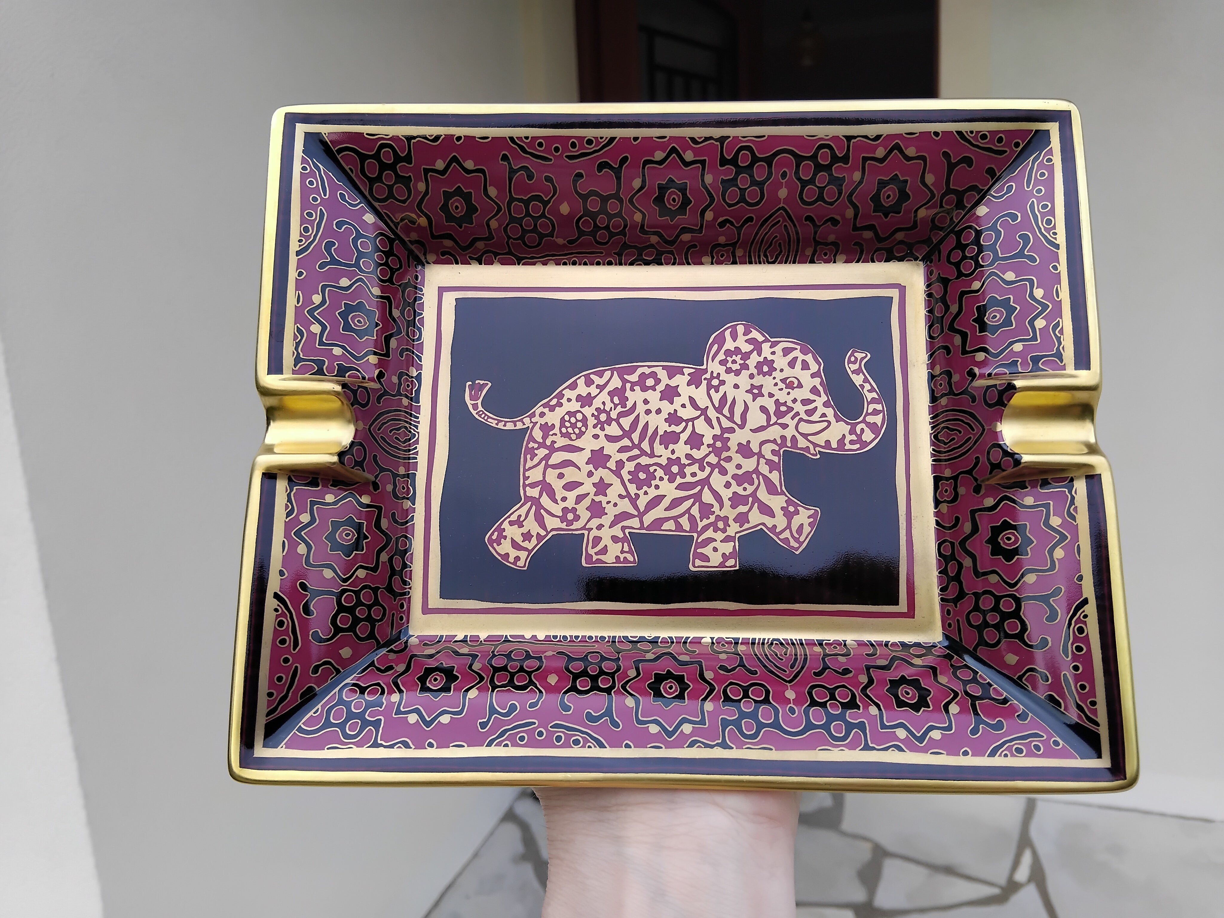 Adorable Authentic Hermès Ashtray

Print: baby elephant

Made in France

Made of porcelain, edges and notches hand painted with fine yellow gold

Colorways: raspberry pink, gold, black

Beige suede leather at bottom, 