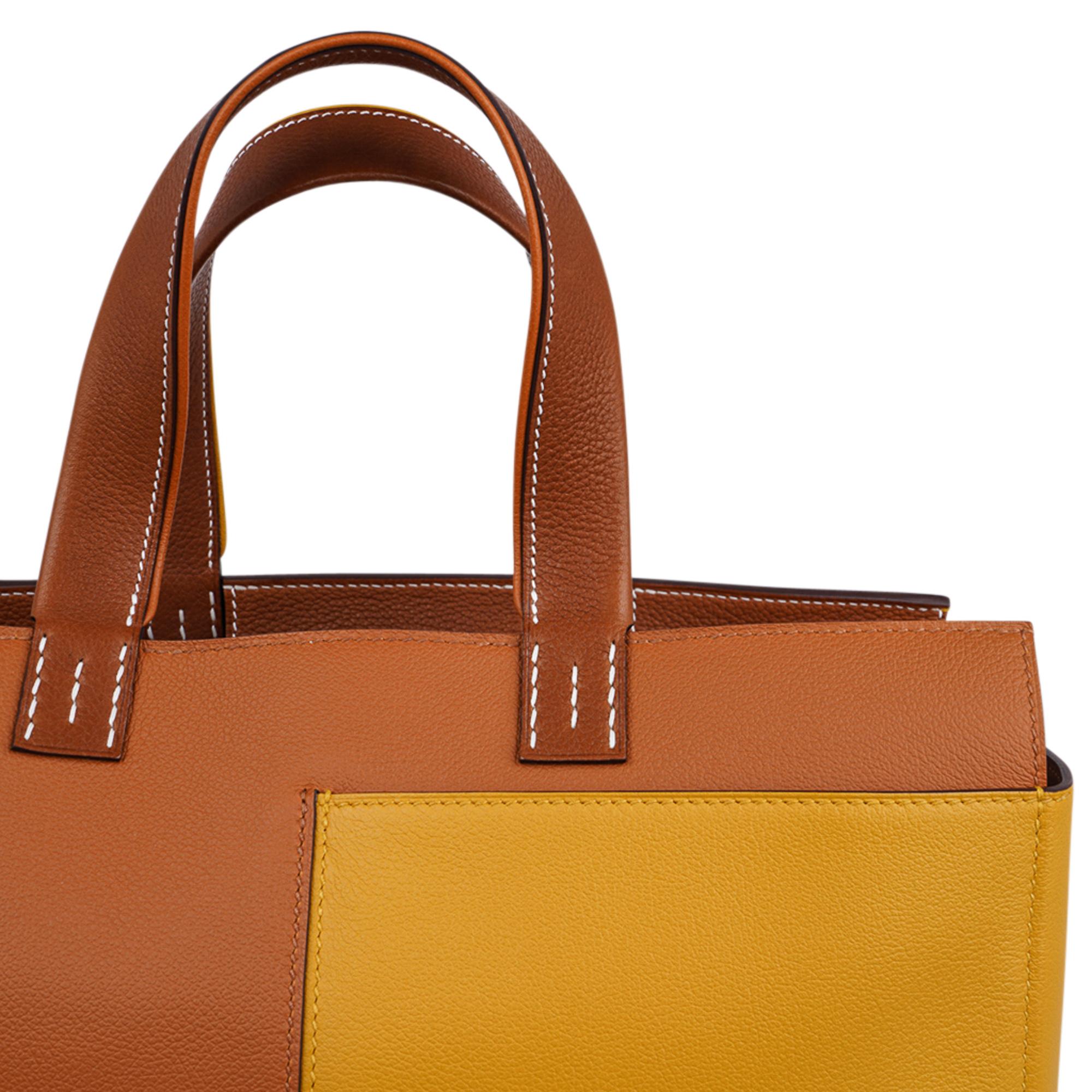 Mightychic offers a guaranteed authentic Hermes Necto 34 Tote is featured in Toffee and Jaune Ambre.
The front has two exterior slot pockets.
The Necto 34 bag comes in Evercolor leather and palladium hardware.
Two handles. one trimmed in Toffee and