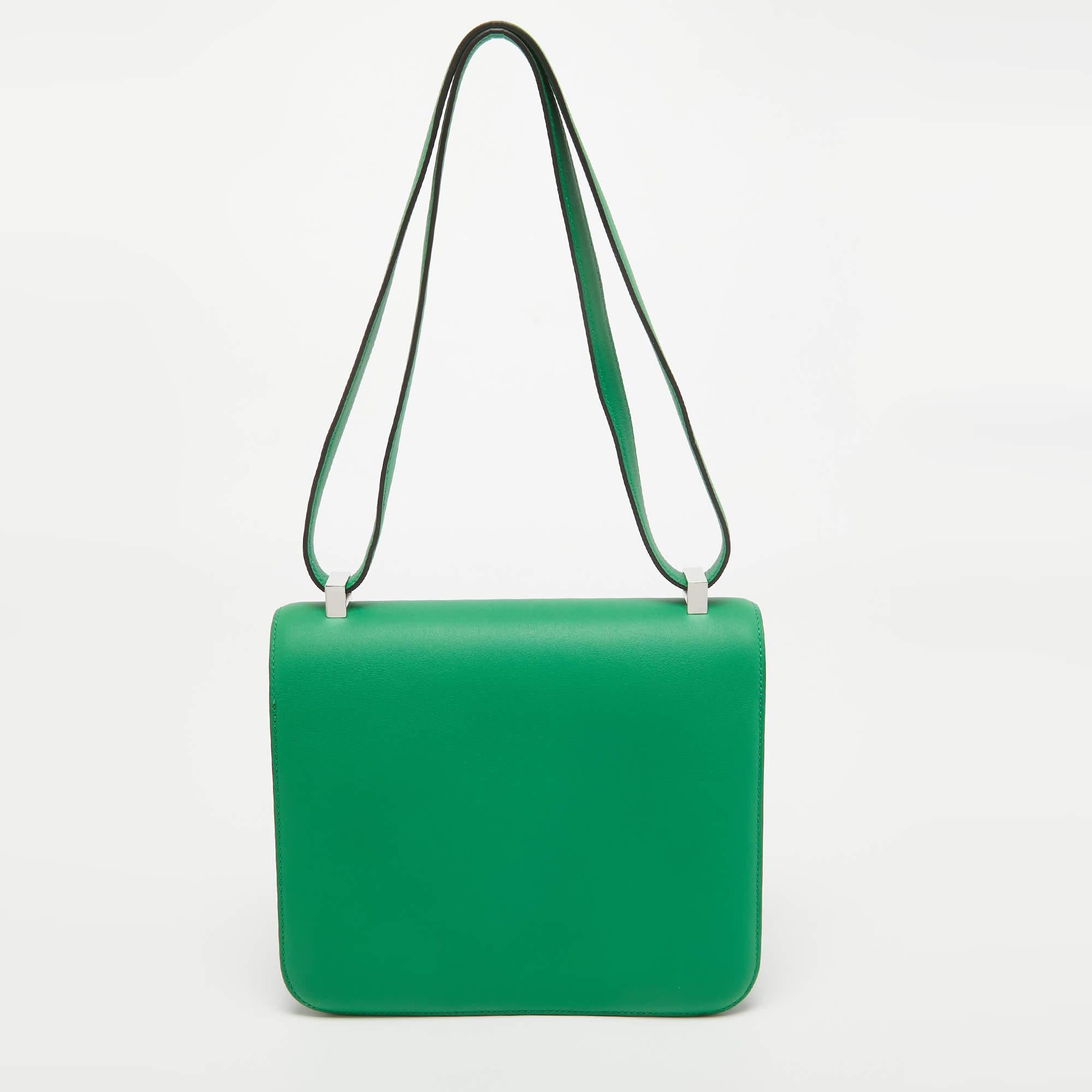 The Hermès Constance Bag features exquisite craftsmanship with a sleek bamboo green hue in supple Swift leather. Accented by Palladium finish hardware, its iconic H-shaped clasp opens to a compact interior, making it a timeless and sophisticated