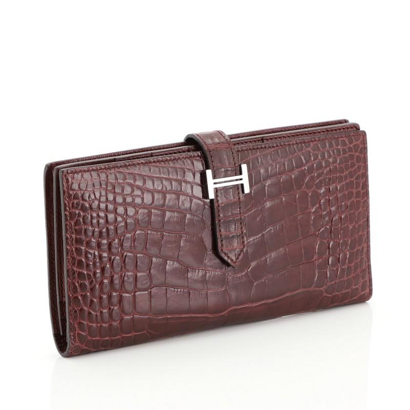 This Hermes Bearn Wallet Matte Alligator Long, crafted from genuine Bordeaux red Shiny Alligator, features palladium hardware. Its tab closure opens to a Bordeaux red Chevre leather interior with multiple card slots and zip pocket. Date stamp reads: