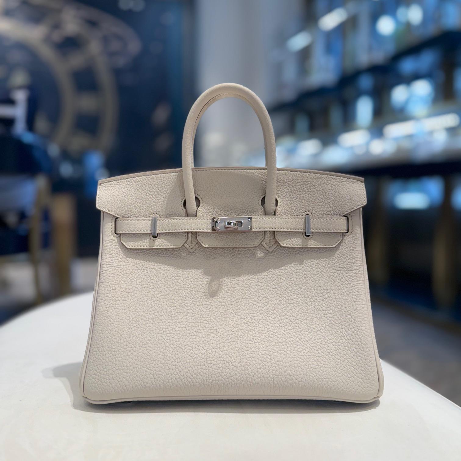 Jewels Aficionado offers the Hermès Birkin 25 in Beton Togo leather, a timeless blend of elegance and versatility. The soft light beige hue with taupe undertones pairs effortlessly with any look, while Togo leather provides a durable, textured