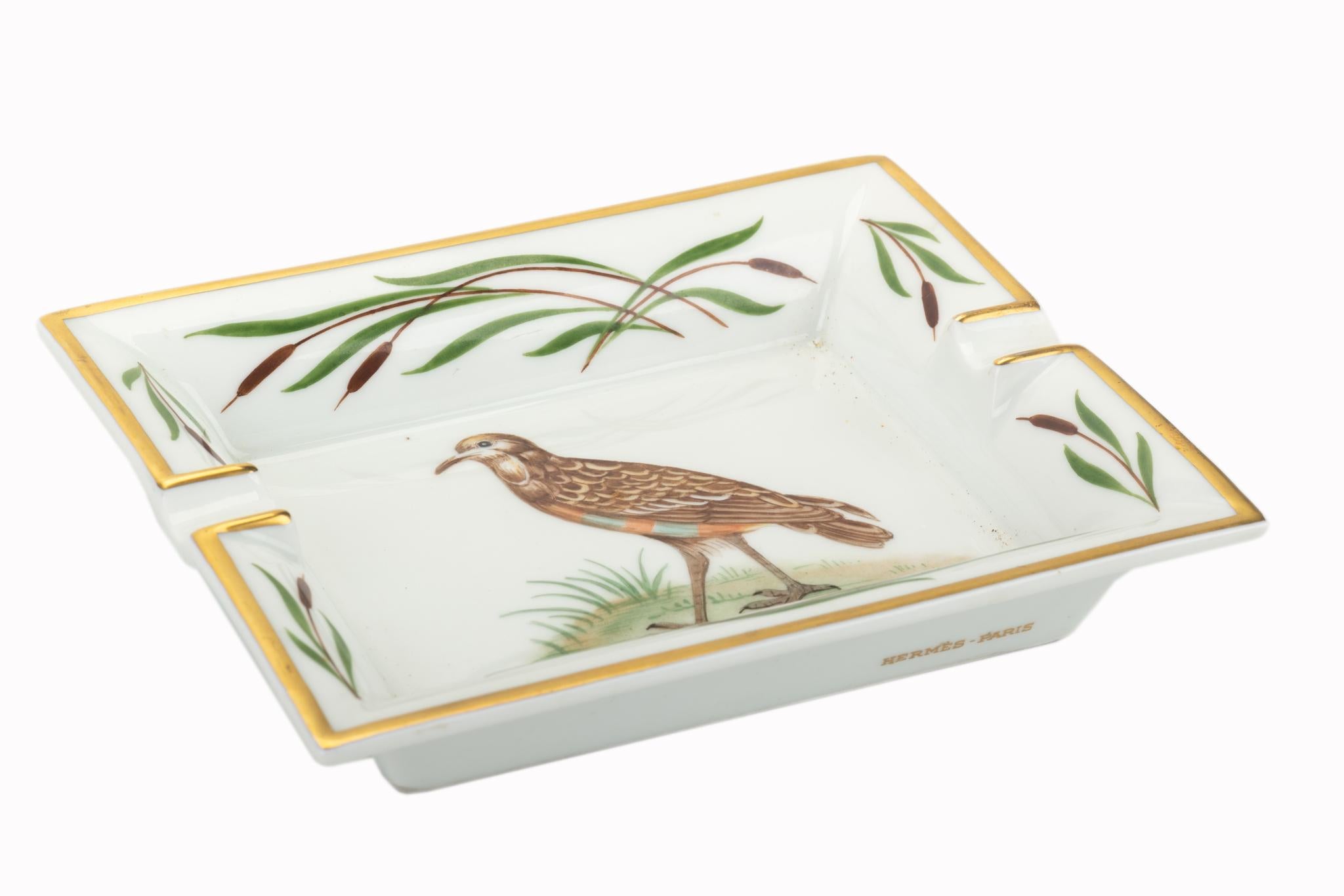 Posacenere firmato Hermes con disegno di uccelli in marrone, giallo e oro. Fondo stampato in pelle scamosciata. Prodotto in Francia.
