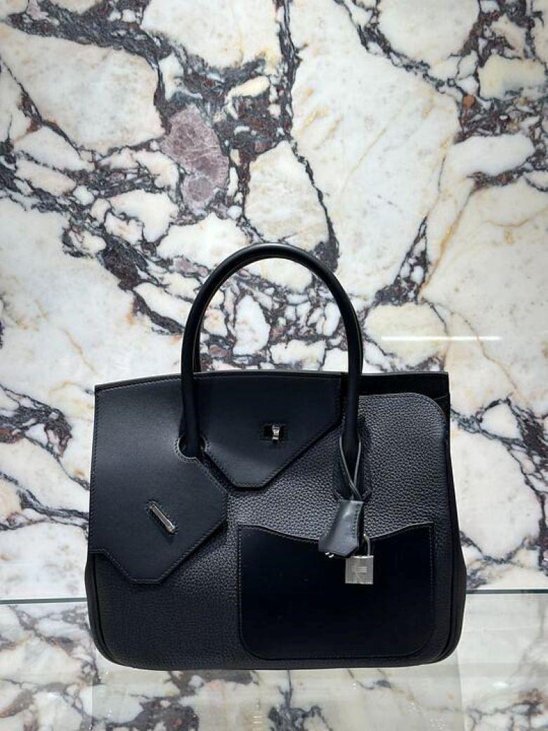 Jewell Aficionado propose un Hermès Birkin 30 en cuir Veau Desordre Noir Togo et Swift, une pièce étonnante et distinctive qui allie sophistication et touche d'unicité. Le Veau Desordre Noir, un noir profond et sombre avec une finition riche et