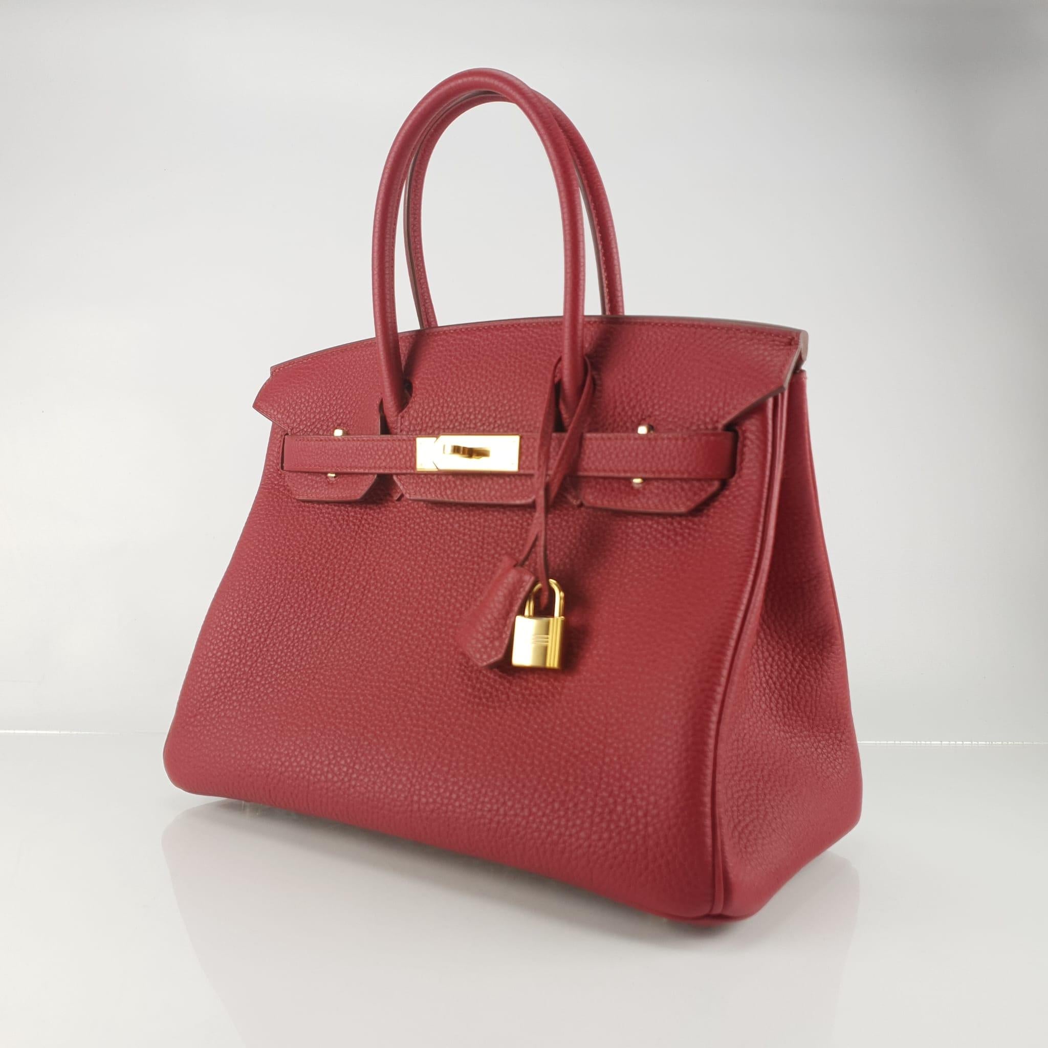 Classic Birkin rendered in Ruby red Togo leather and accented with gold-plated hardware. Togo leather is a thick and durable calfskin with a medium grain known for its resilience to scratches and ability to be repaired easily. Includes lock, two