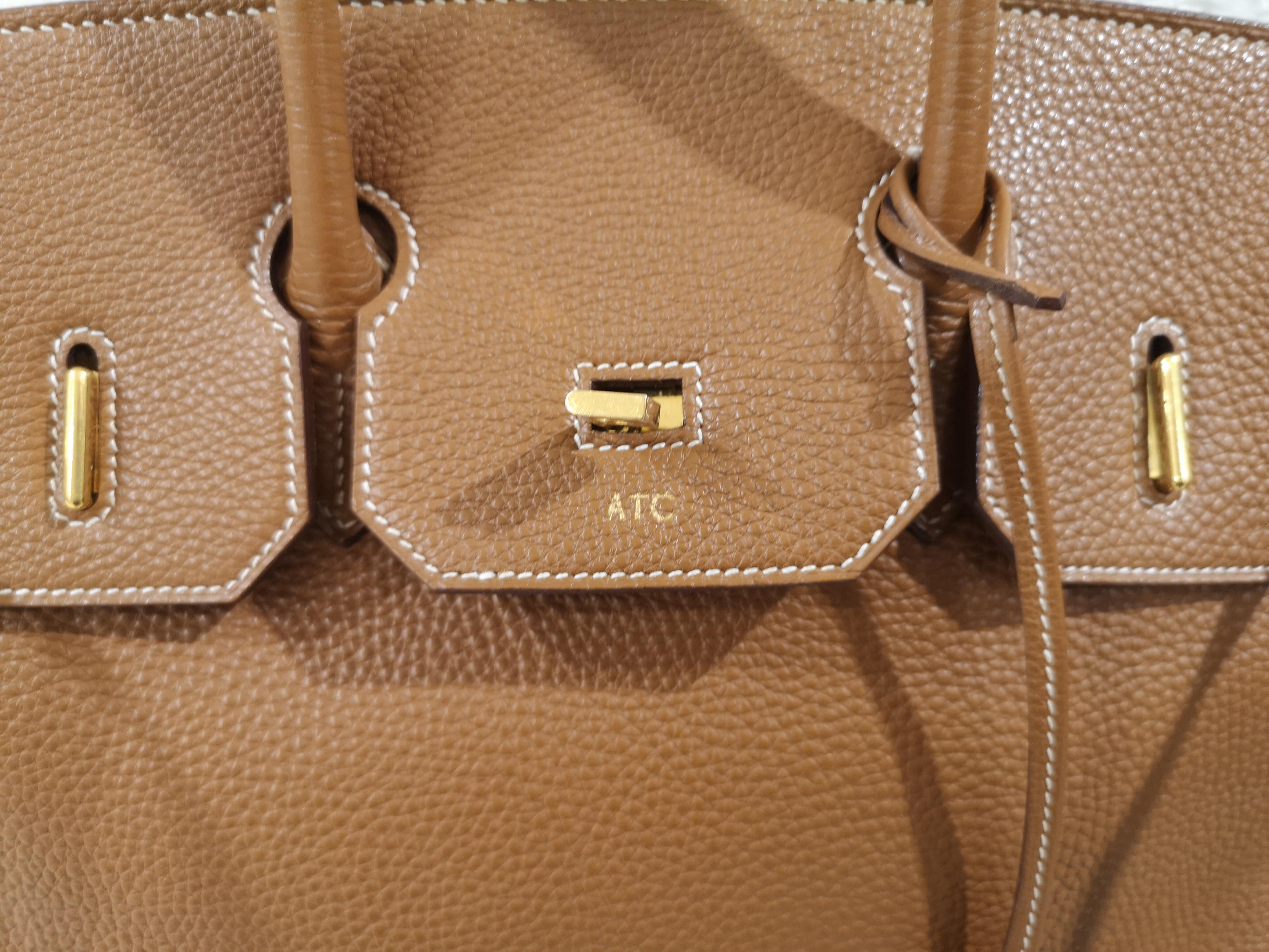 Hermès Courchevel HAC Birkin 32 Gold customized ATC capital letter on the front  This luxury classic is crafted of grained Courchevel calfskin leather in golden camel brown. The bag features rolled top handles, a strap closure, and a gold plated