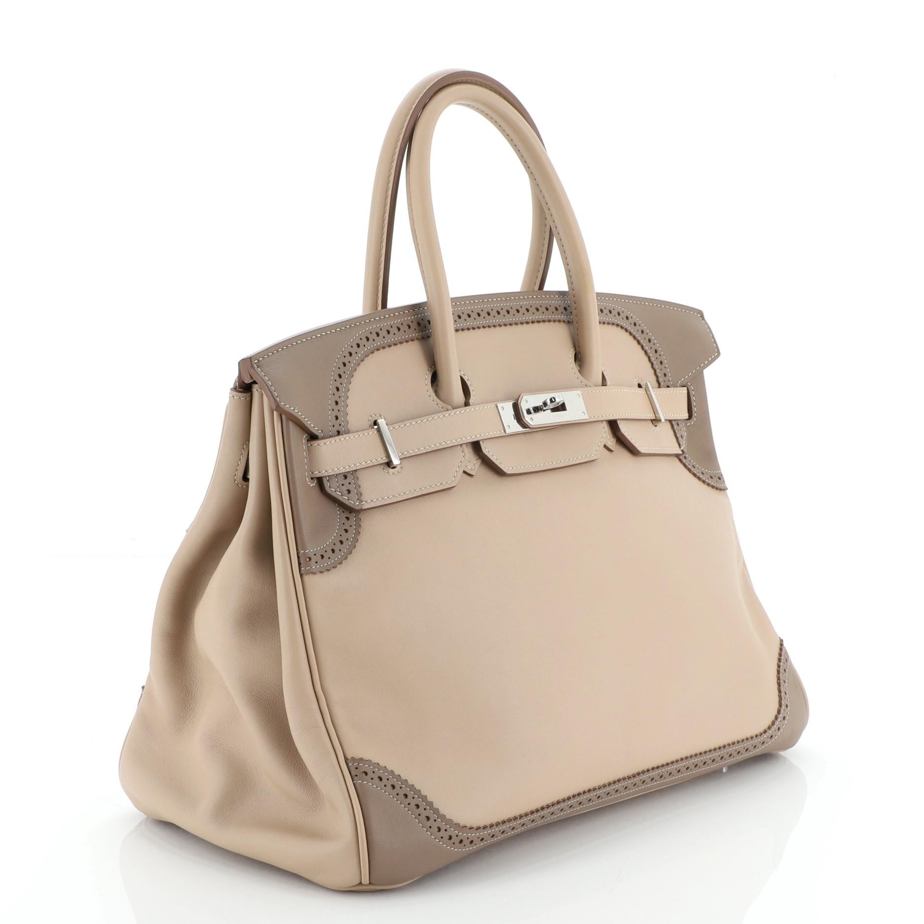This Hermes Birkin Ghillies Handbag Argile and Etoupe Swift with Palladium Hardware 35, crafted from Argile and Etoupe Swift leather, features a single looped top handle, broguing at top and bottom, protective base studs, and palladium hardware. Its