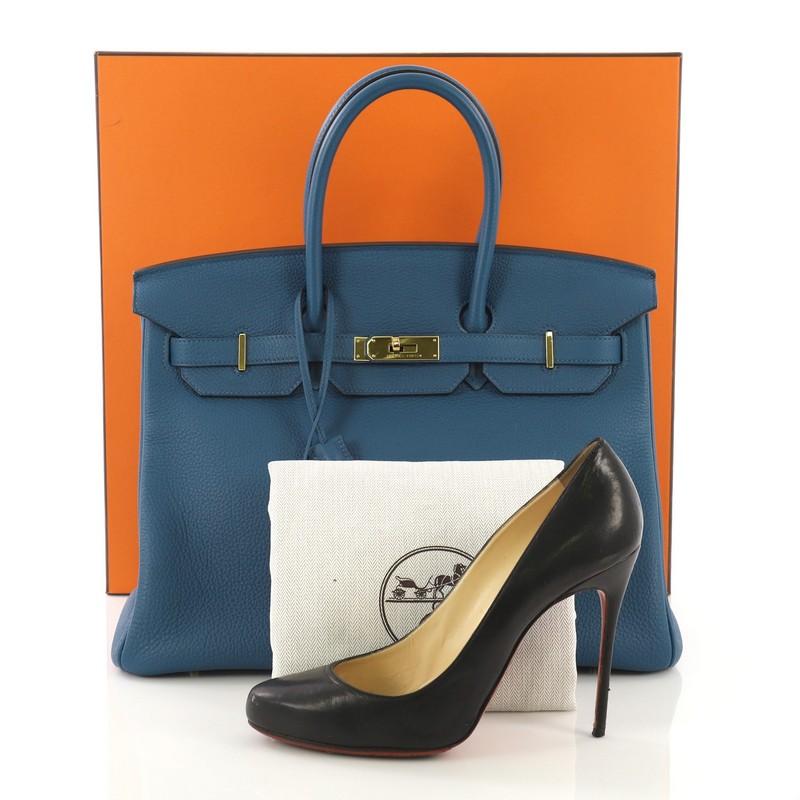 This Hermes Birkin Handbag Bleu de Galice Togo With Gold Hardware 35, crafted in Bleu de Galice blue Togo leather, features dual rolled handles, frontal flap, and gold hardware. Its turn-lock closure opens to a Bleu de Galice blue Chevre leather