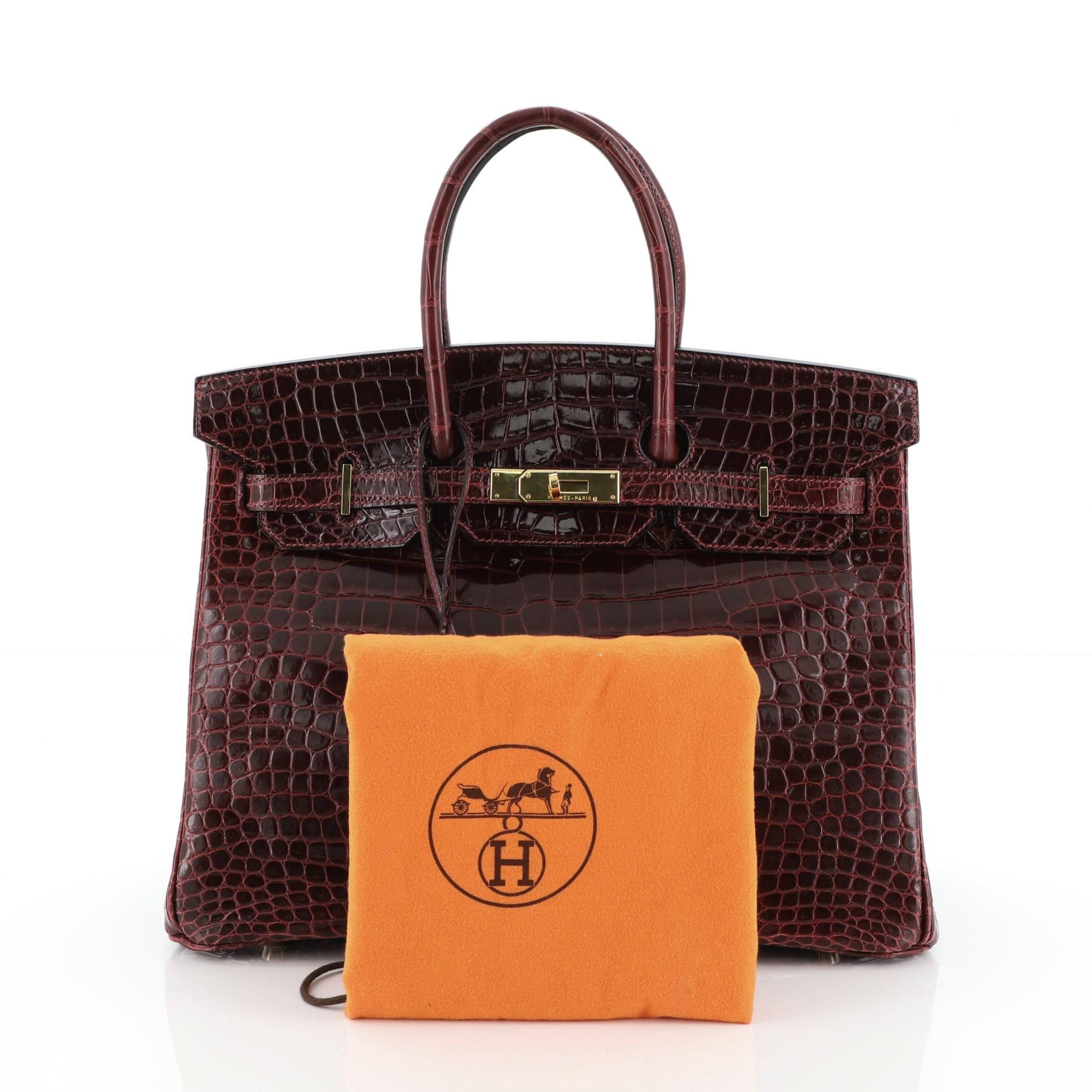 This Hermes Birkin Handbag Bordeaux Shiny Porosus Crocodile with Gold Hardware 35, crafted in genuine Bordeaux red Shiny Porosous Crocodile, features dual rolled handles, frontal flap, and gold hardware. Its turn-lock closure opens to a Bordeaux red