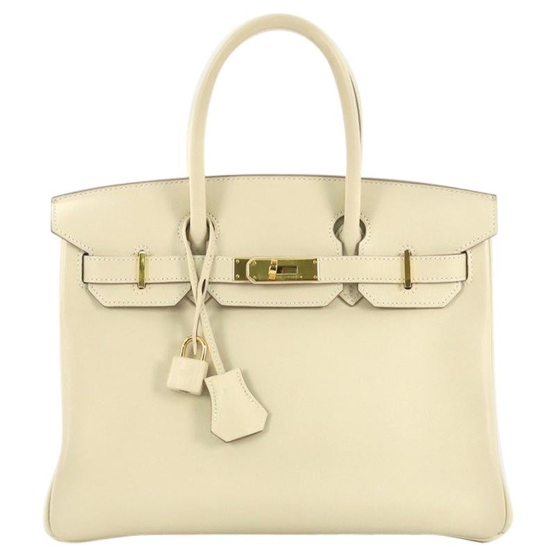 This Hermes Birkin Handbag Craie Swift with Gold Hardware 30, crafted in Craie beige Swift leather, features dual rolled handles, frontal flap, and gold hardware. Its turn-lock closure opens to a Craie beige Swift leather interior with slip pocket.