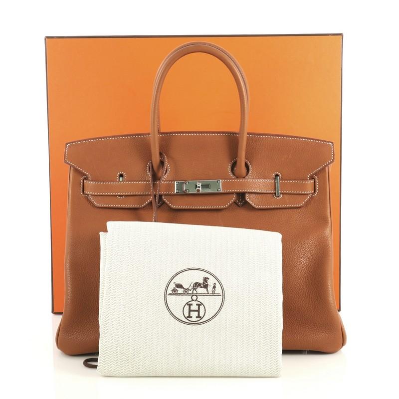 This Hermes Birkin Handbag Fauve Barenia Faubourg with Palladium Hardware 35, crafted in Fauve brown Barenia Faubourg leather, features dual rolled top handles, frontal flap, and palladium hardware. Its turn-lock closure opens to a Fauve brown