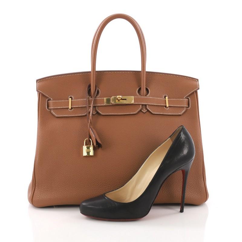 This Hermes Birkin Handbag Gold Togo with Gold Hardware 35, crafted in gold brown togo leather, features dual rolled handles, front flap and gold-tone hardware. Its turn-lock closure opens to a brown leather interior with slip and zip pockets. Date