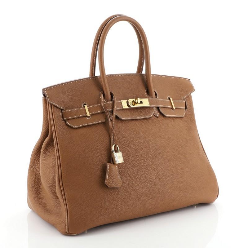 This Hermes Birkin Handbag Gold Togo with Gold Hardware 35, crafted in Gold brown Togo leather, features dual rolled top handles, frontal flap, and gold hardware. Its turn-lock closure opens to a Gold brown Chevre leather interior with zip and slip