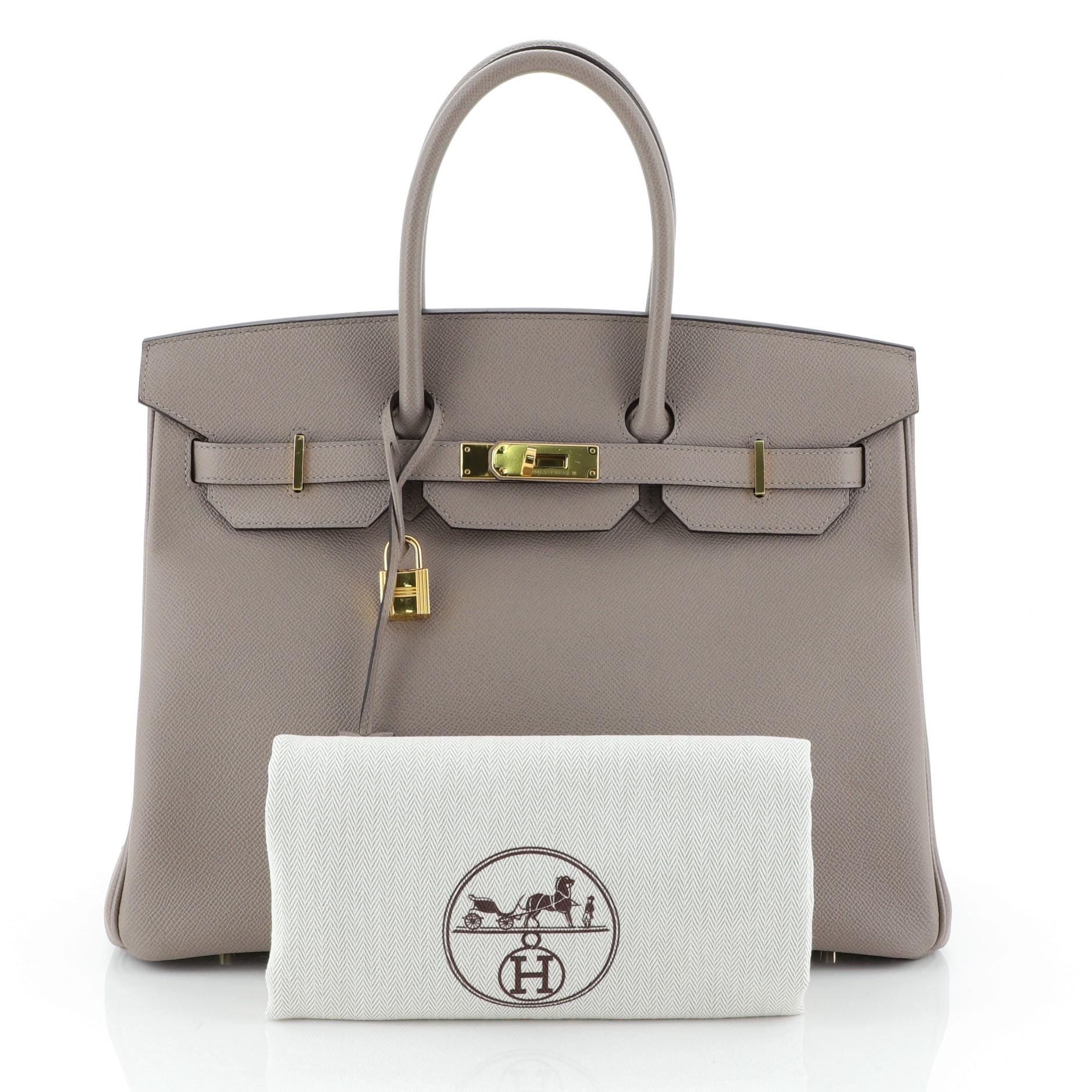 This Hermes Birkin Handbag Gris Asphalte Epsom with Gold Hardware 35, crafted in Gris Asphalte gray Epsom leather, features dual rolled handles, frontal flap, and gold hardware. Its turn-lock closure opens to a Gris Asphalte gray Chevre leather